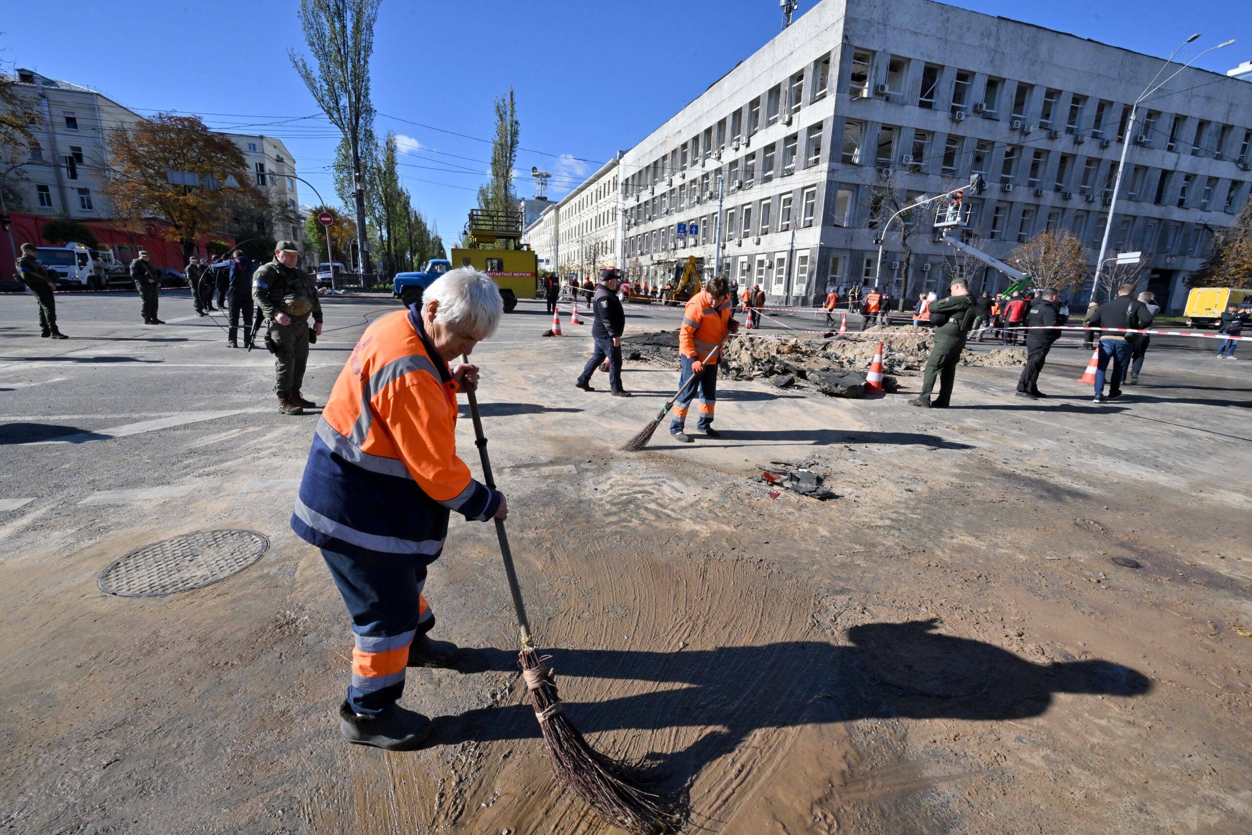 City workers clean the asphalt next to a rocket crater in central Kyiv on October 10, 2022 after Ukraine's capital was hit by multiple Russian strikes early on today, the first since late June. - The head of the Ukrainian military said that Russian forces launched at least 75 missiles at Ukraine, with fatal strikes targeting the capital Kyiv, and cities in the south and west. (Photo by Sergei SUPINSKY / AFP)