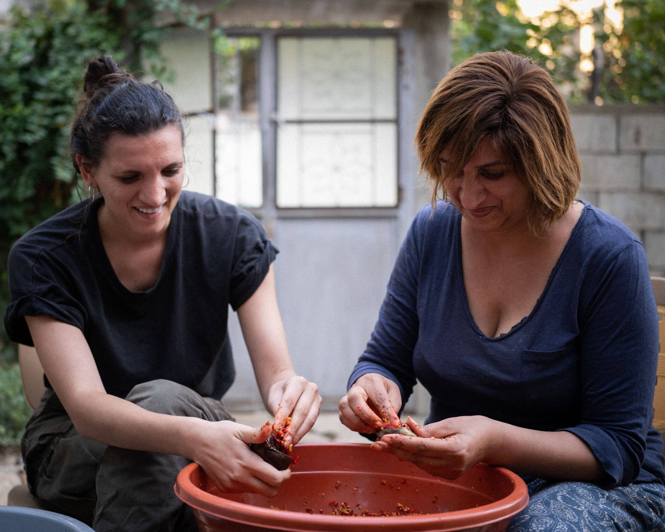 dwie kobiety obierają papryczki nad glinianą misą
