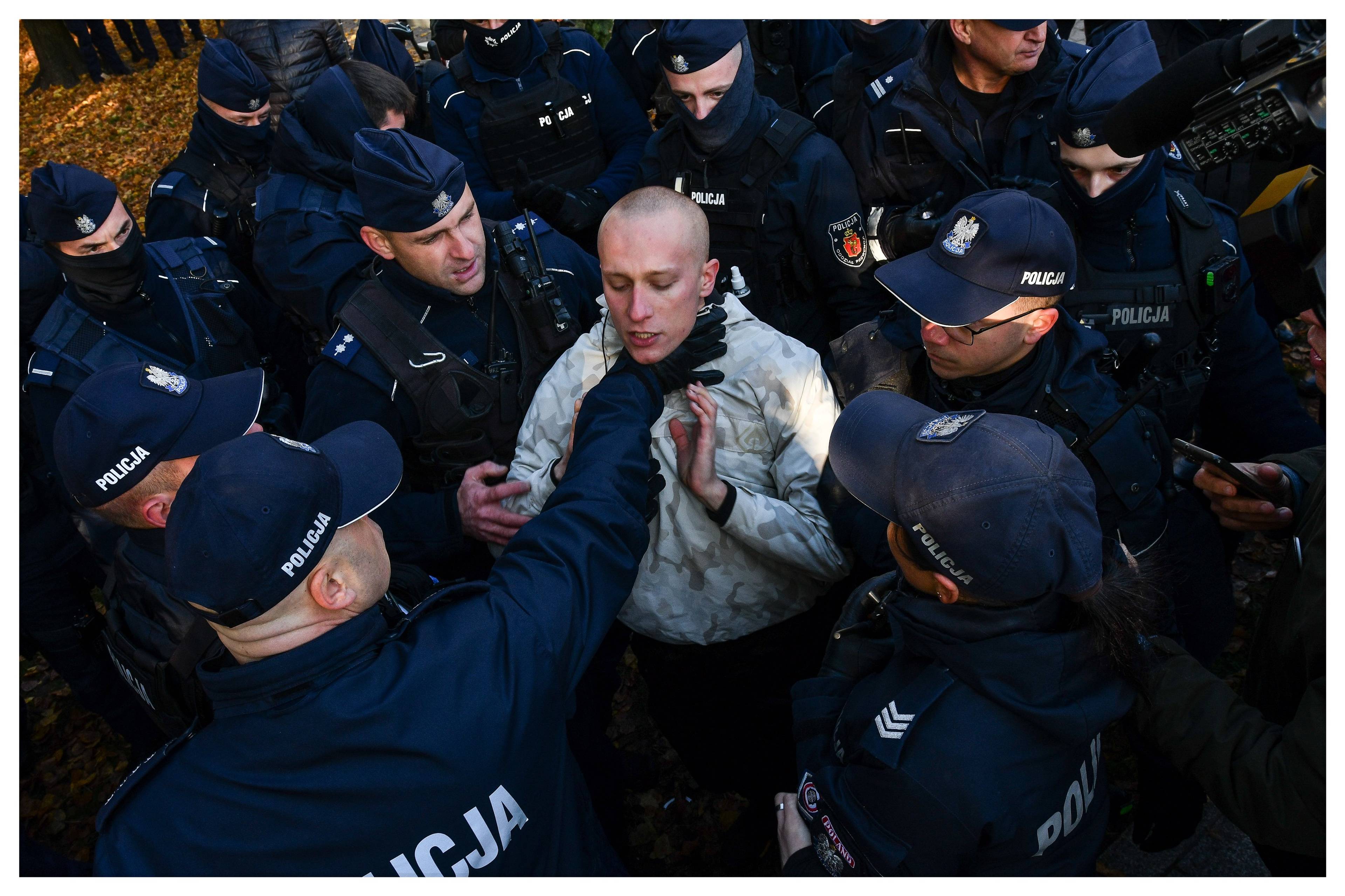 Policjant chwyta za gardło protestującego, otoczonego przez innych policjantów. Policyjna przemoc