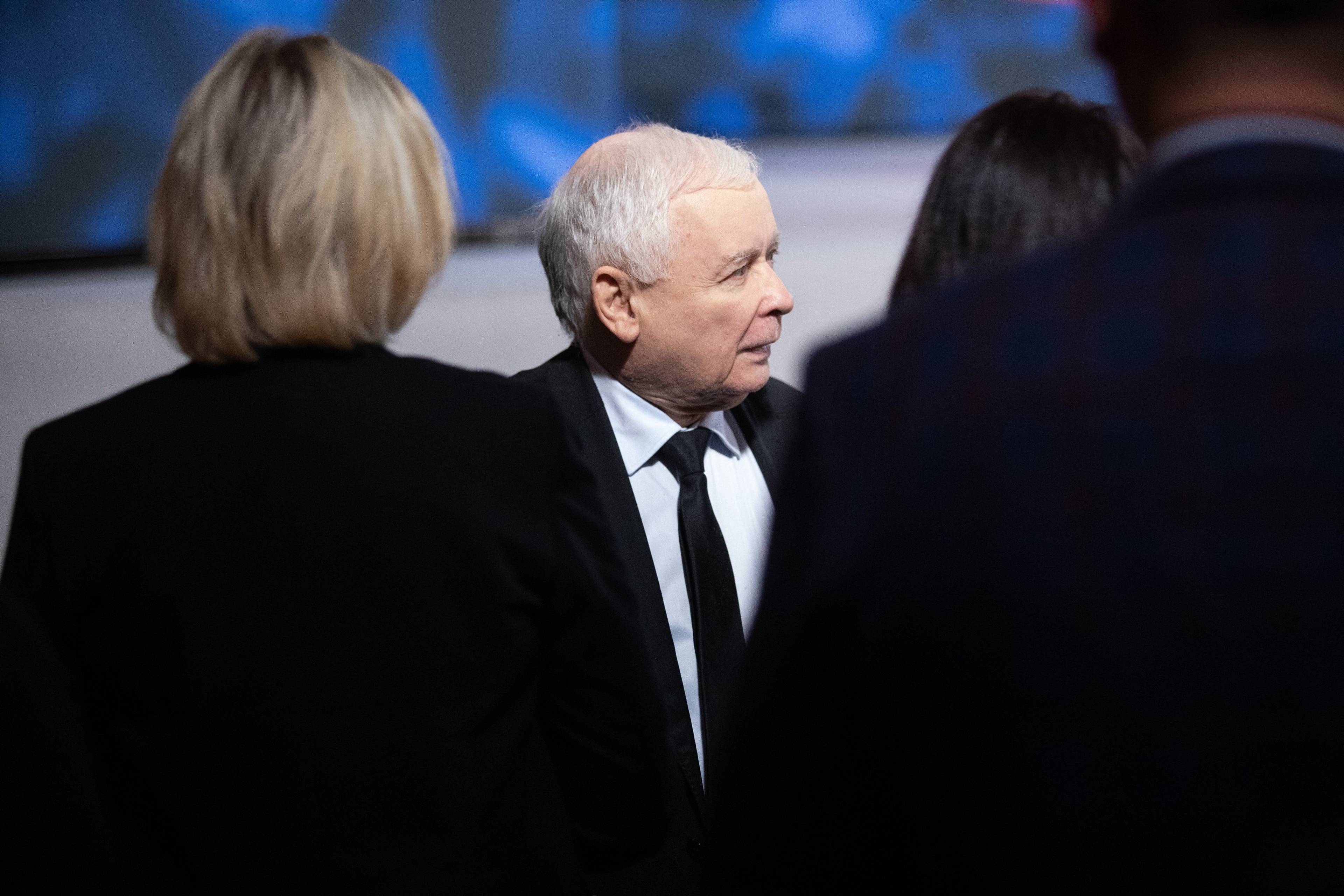 Prezes PiS Jarosław Kaczyński przesłonięty przez odwrócone plecami do kadru dwie kobiety
