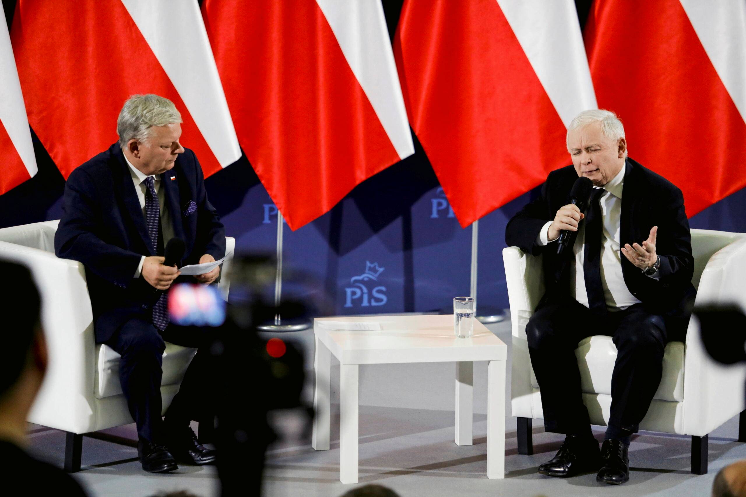 na fotelach, na tle polskich flag, siedzą: z lewej Marek Suski, z prawej - Jarosław Kaczyński
