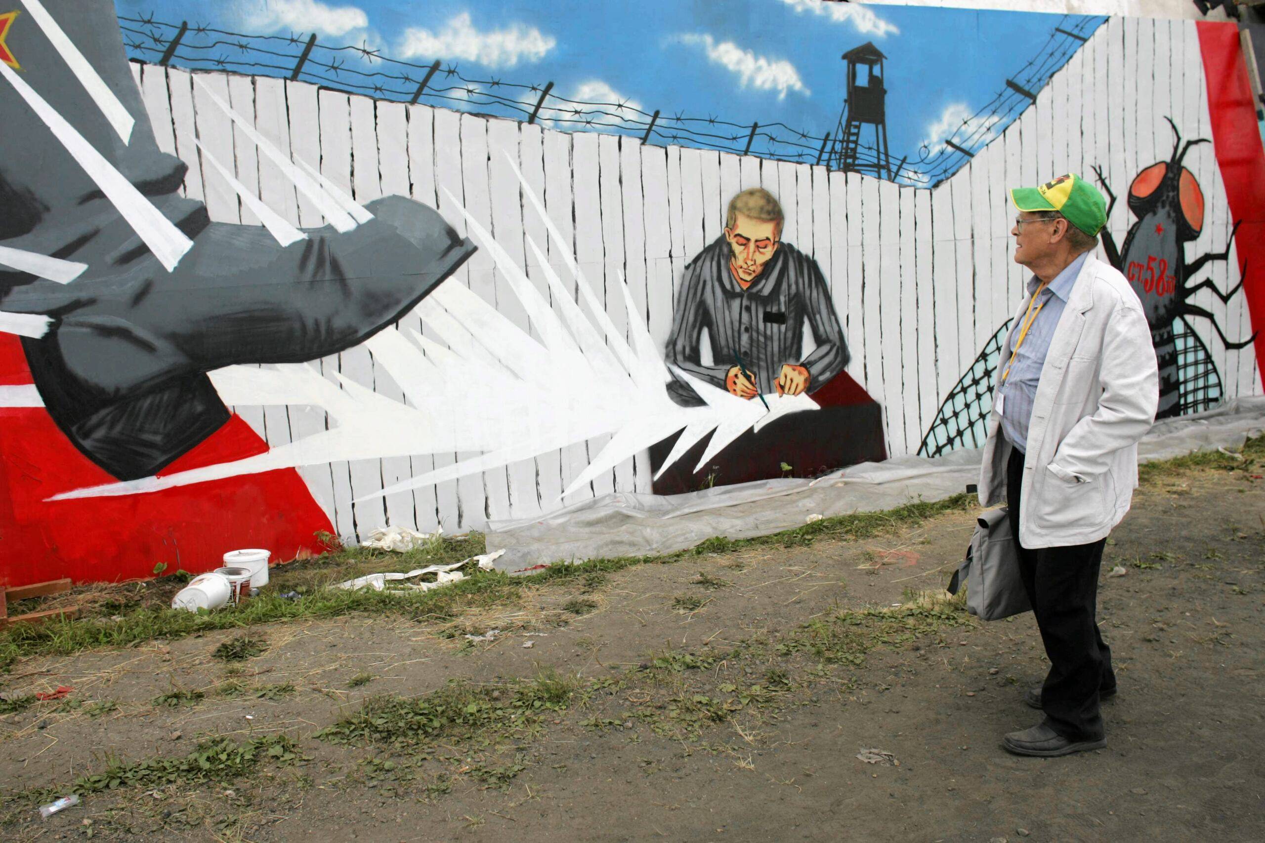 metalowy płot z graffitti, przedstawiającego więźnia który pisze pamietnik