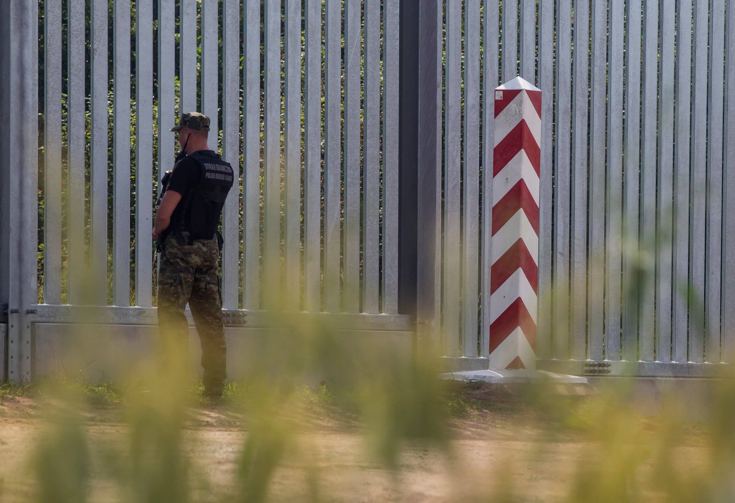 Mur graniczny, polski słup graniczny i funkcjonariusz polskiej straży granicznej