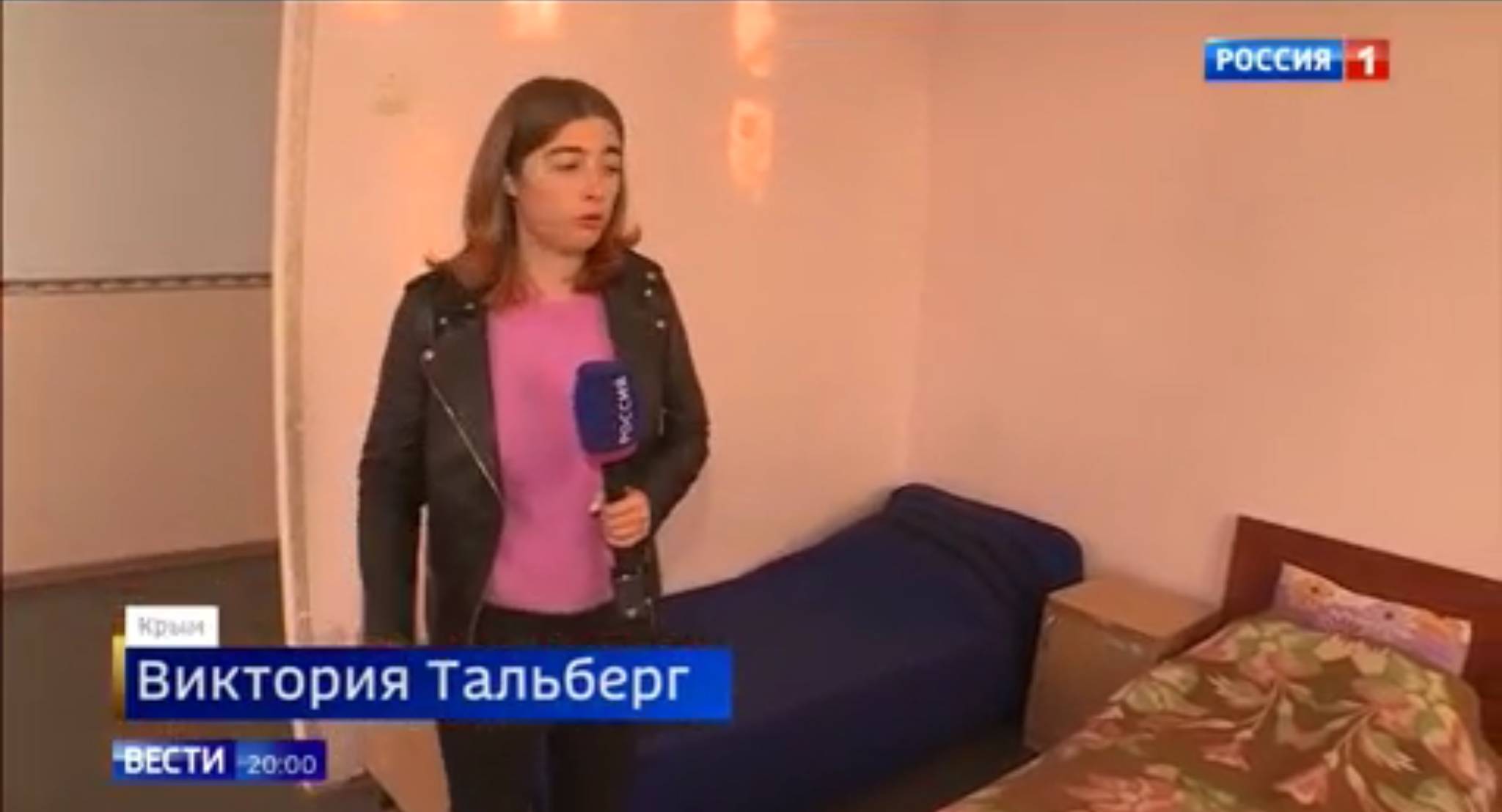 Kobieta z mikrofonem pokazuje pusty pokój z kilkoma łóżkami