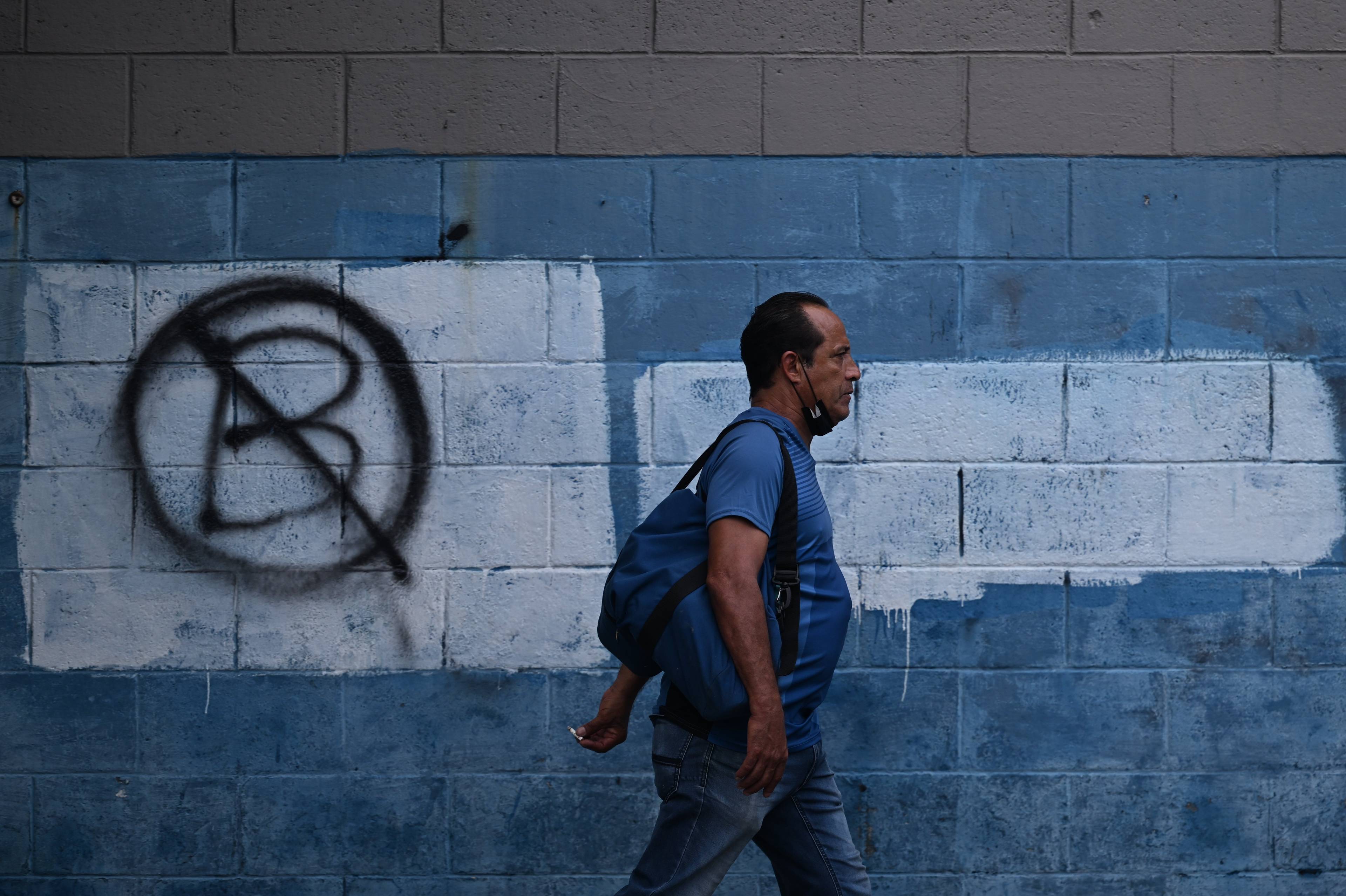 A man walks past a wall painted with an anti-bitcoin protest symbol, in San Salvador, on October 18, 2022. - Most Salvadorans have not used bitcoin so far this year and consider that the emblematic bet of President Nayib Bukele has been a failure, assured Tuesday a poll of the private Central American University (UCA, Jesuit). (Photo by Marvin RECINOS / AFP)