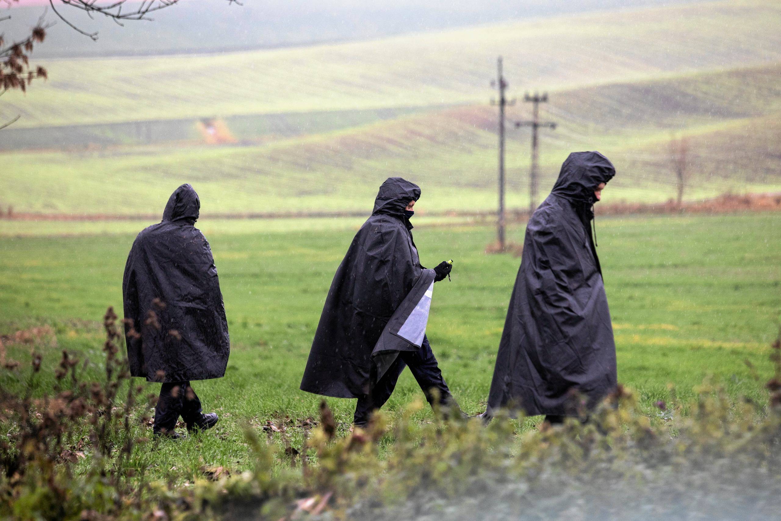 Trzy postaci w ciemnych płaszczach z kapyirami chodzą po zielonym polu