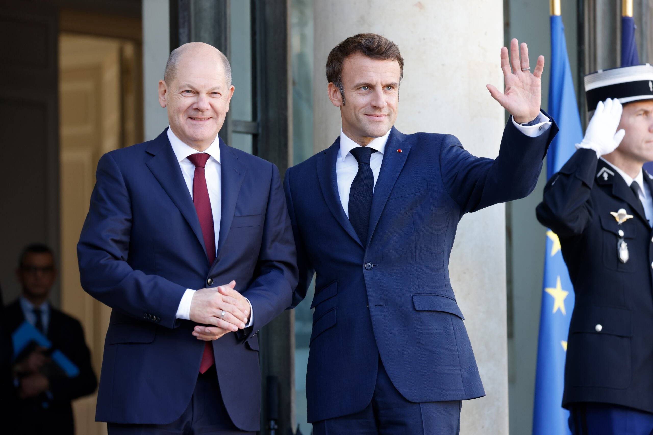 France's President Emmanuel Macron (R) waves as he welcomes German Chancellor Olaf Scholz upon his arrival for a lunch at the presidential Elysee Palace in Paris on October 26, 2022. - The two leaders aim to "strengthen Franco-German cooperation" and respond to common challenges in a "united and supportive way", to revive the Franco-German tandem, plagued by a series of disputes, from energy to defense, against the backdrop of the war in Ukraine. (Photo by Ludovic MARIN / AFP)