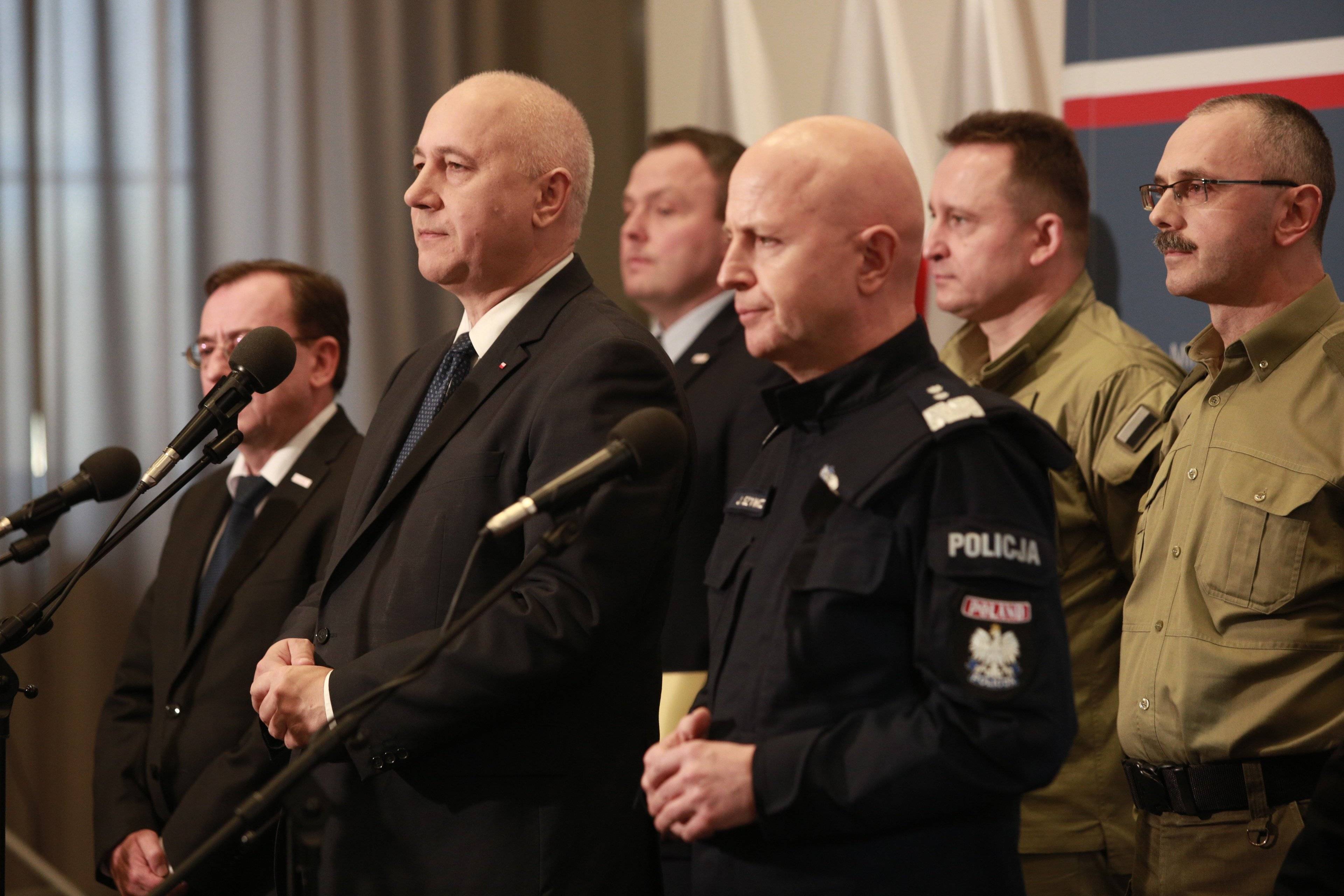 Mężczyźni w dwuszeregu: na pierwszym planie męzczyzna w mundurze policjanta (gen. Szymczyk) i mężczyzna w garniturze (Joachim Brudziński). Z tyłu mężczyźni w garniturze i w mundurach