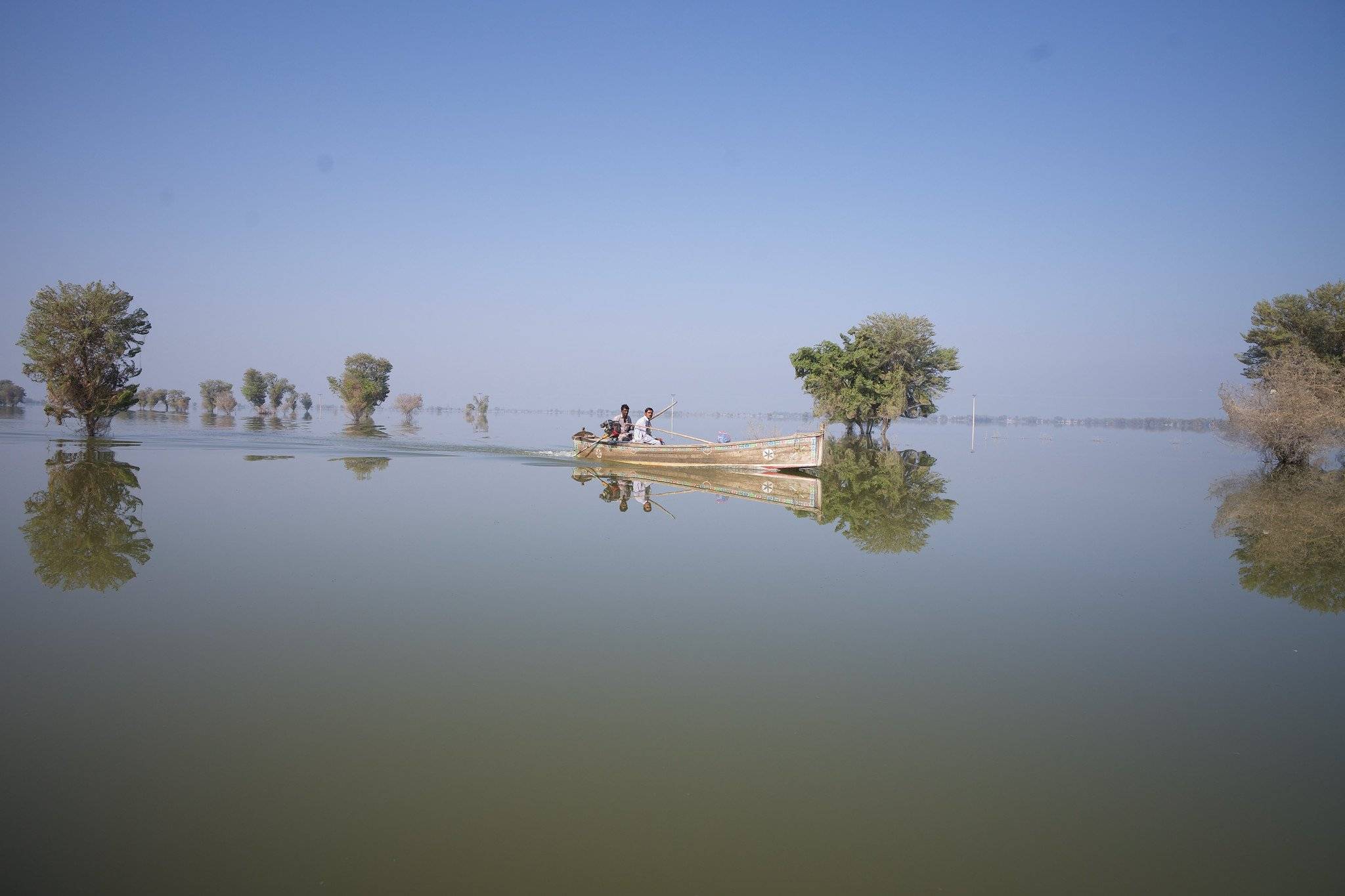 łódka z dwojgiem ludzie na zalanych po horyzont terenach Pakistanu