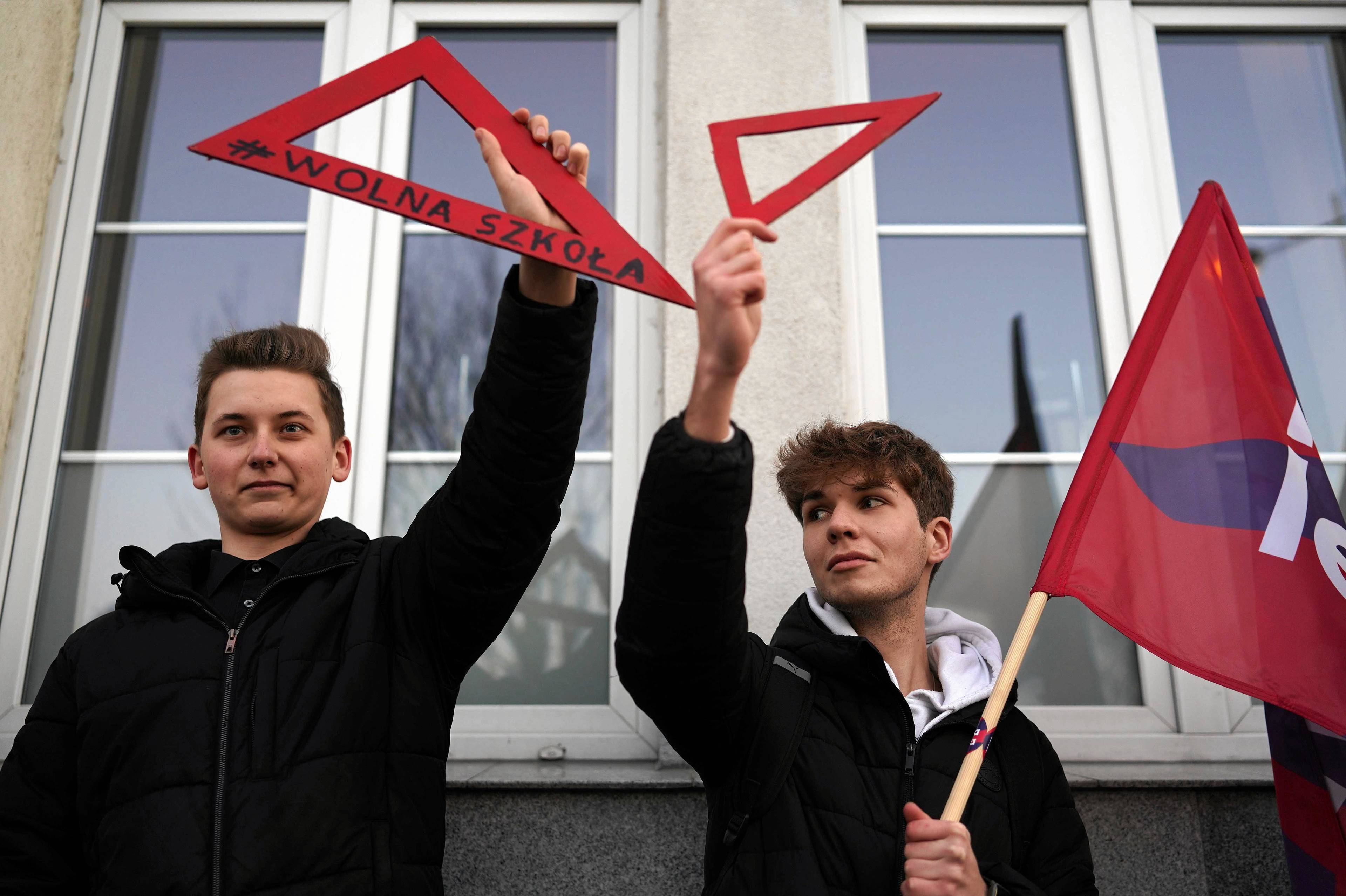 Na zdjęciu dwóch młodych chłopaków podczas manifestacji przeciwko ustawie lex Czarnek. Ubrani w czarne bluzy, w rękach trzymają czerwone ekierki - symbole sprzeciwu wobec szkodliwych zmian w oświacie