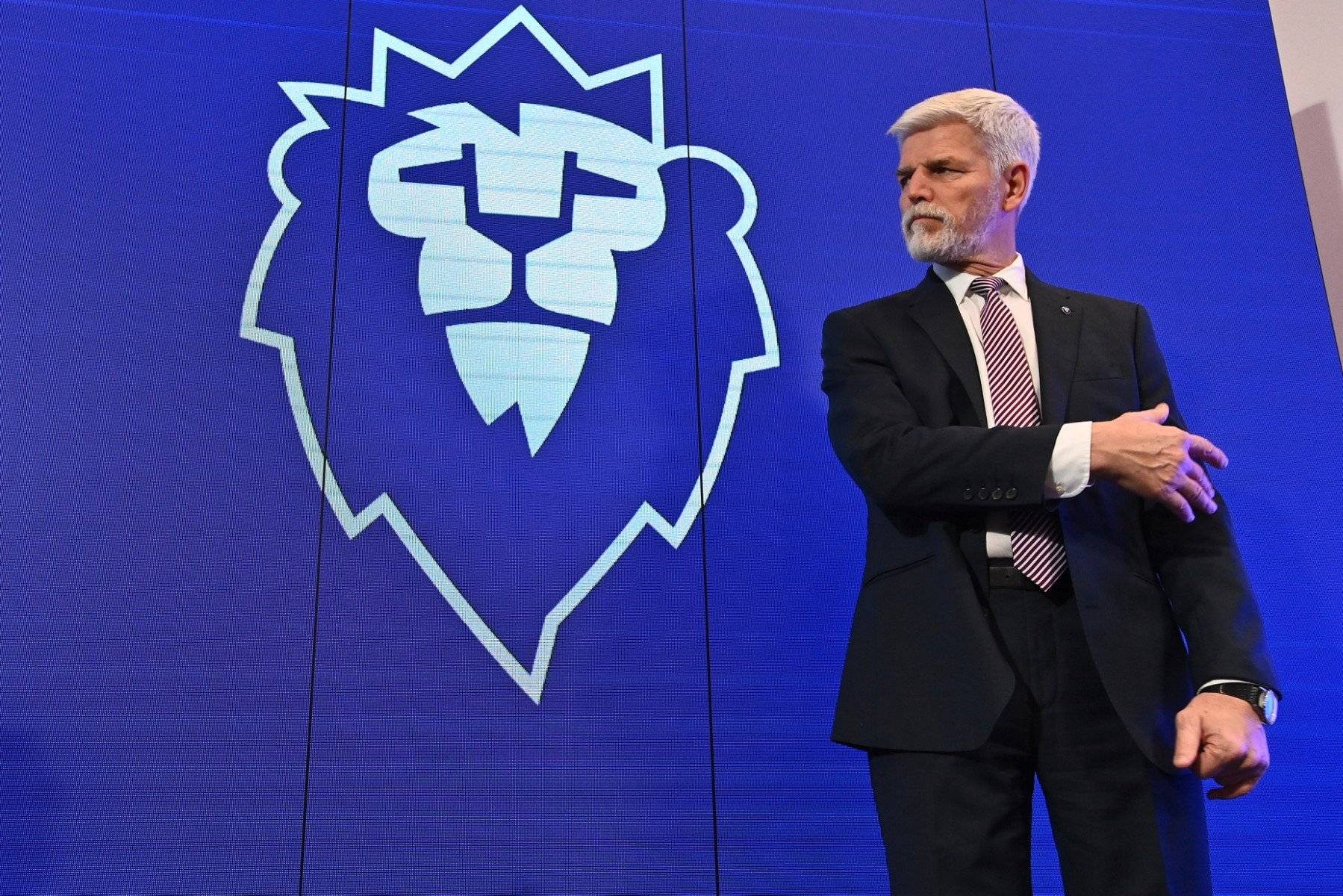 Siwy mężczyzna stoi na tle baneru z naryswaną schematycznie głową lwa