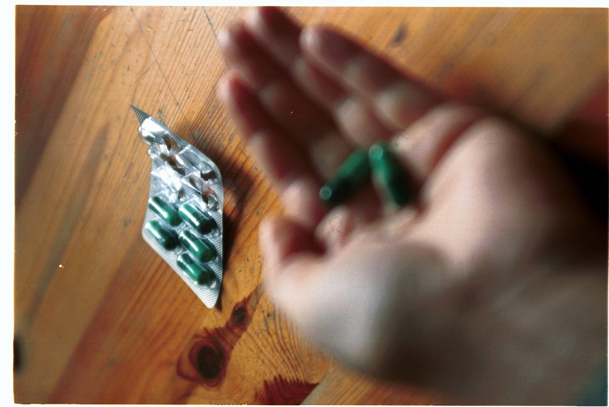 Dłoń trzymająca tabletkę, w tle opakowanie tabletek