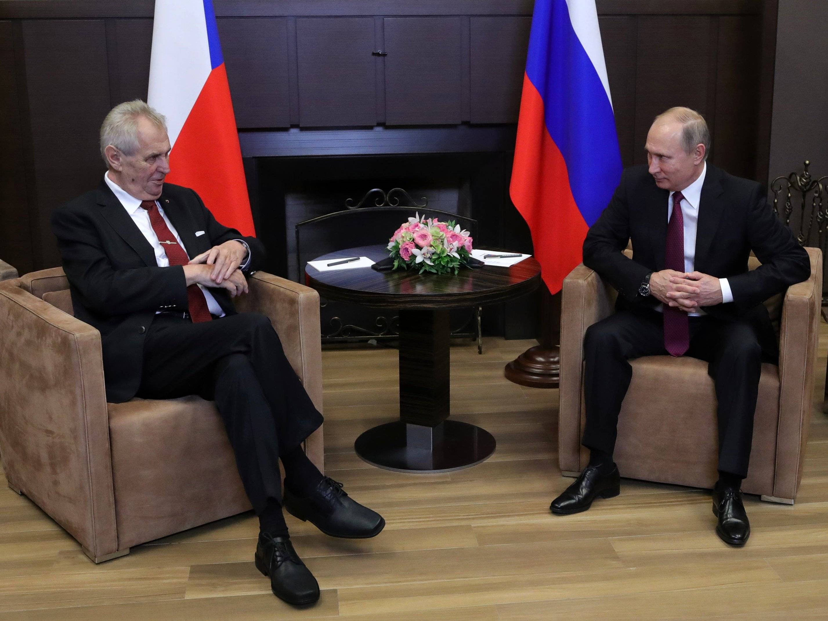Dwaj mezczyźni siedza w fotelach na tle flag Rosji i Czech (Putin i Zeman)