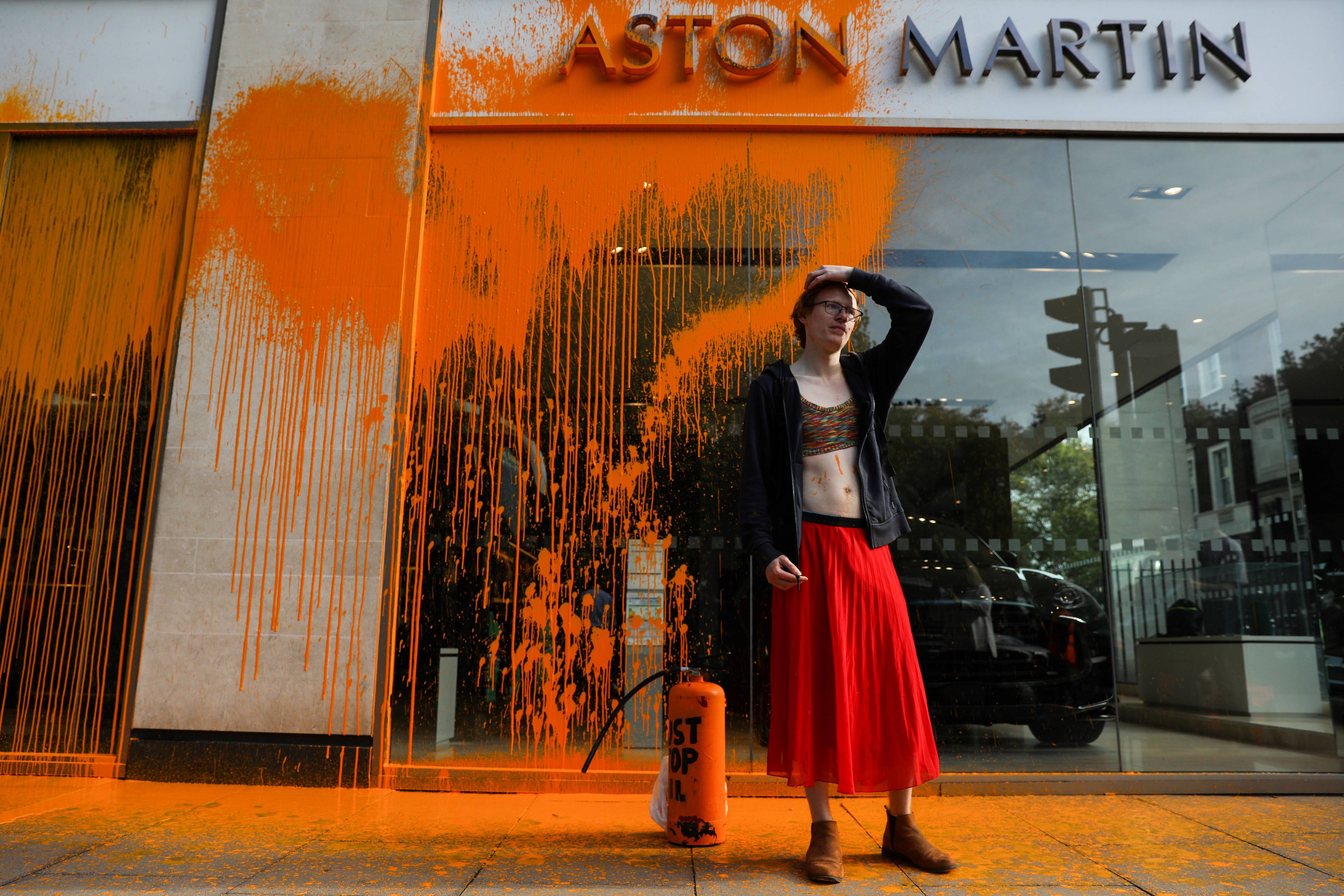 aktywistka na tle pomazanej pomarańczową farbą siedziby Aston Martin