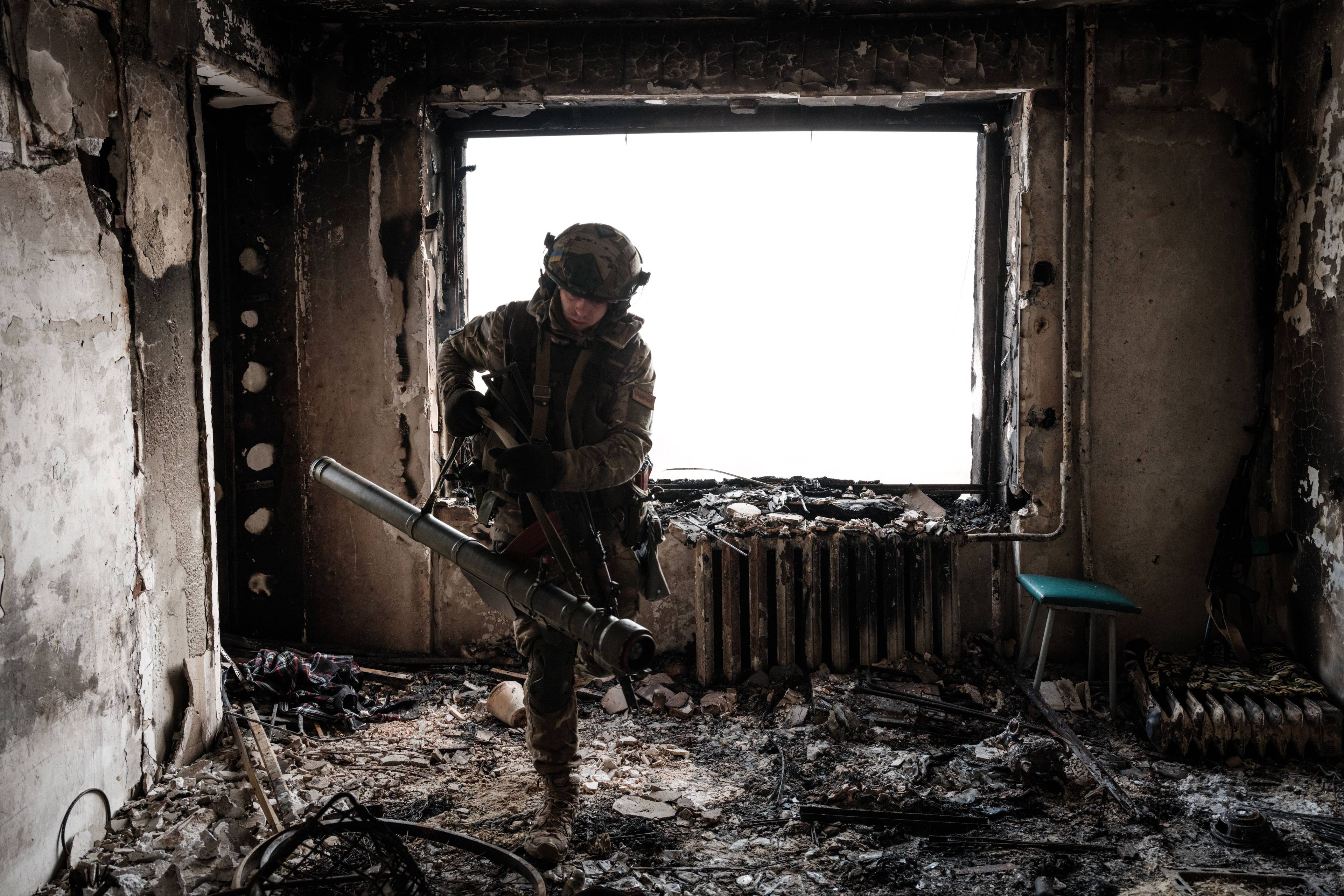 Ukraiński żołnierz w stroju bojowym w zniszczonym mieszkaniu z wybitym oknem w Bachmucie