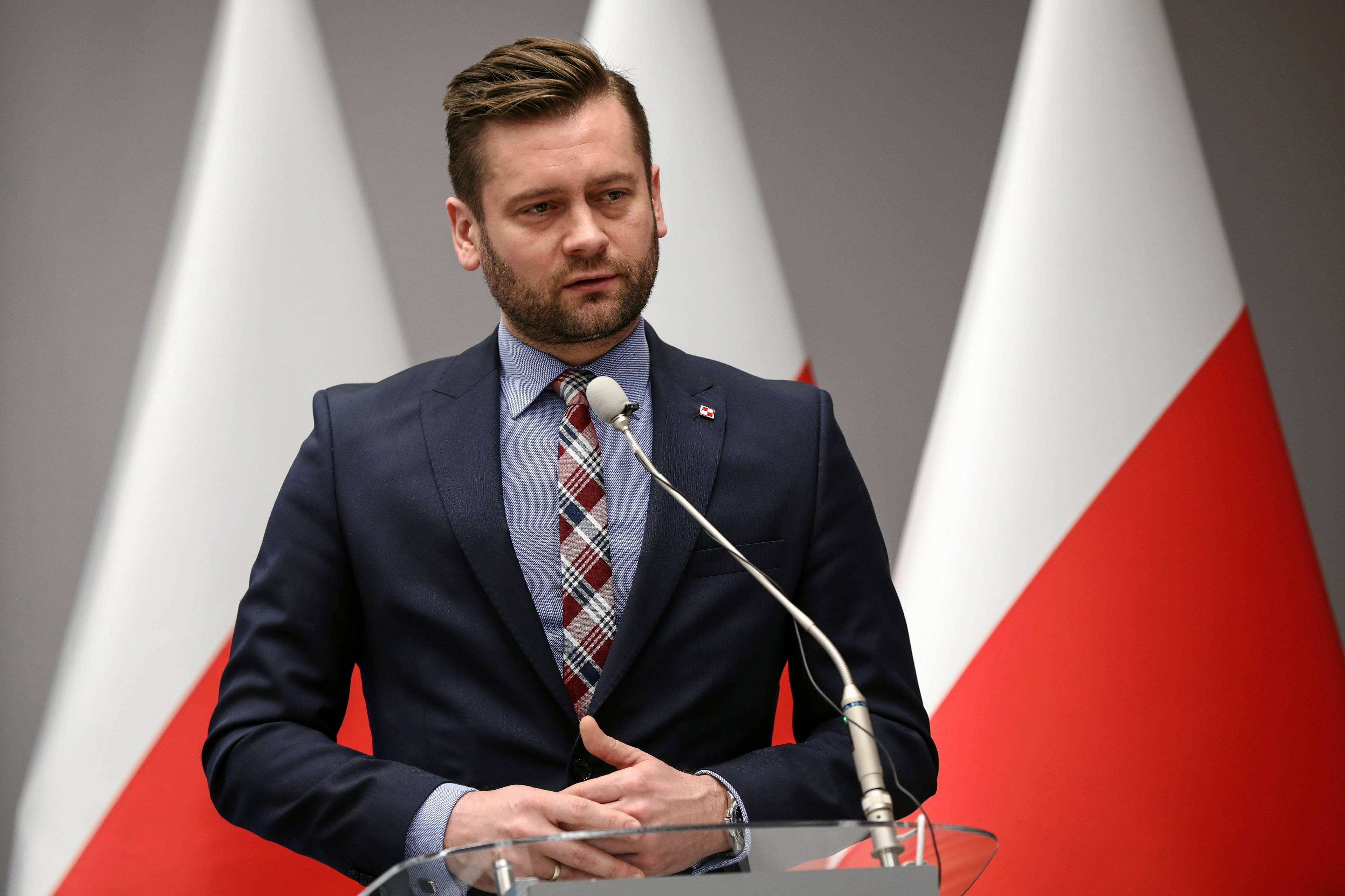 Kamil Bortniczuk - minister sportu w garniturze na tle flag Polski