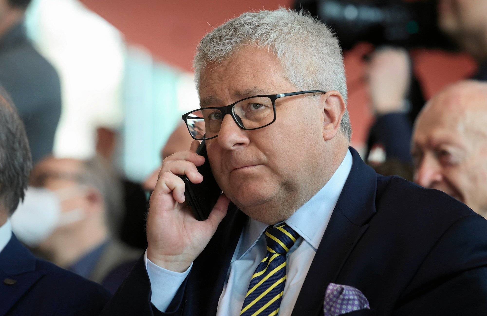 Ryszard Czarnecki w ciemnej marynarce i krawacie w granatowo-żółte paski rozmawia przez telefon komórkowy.