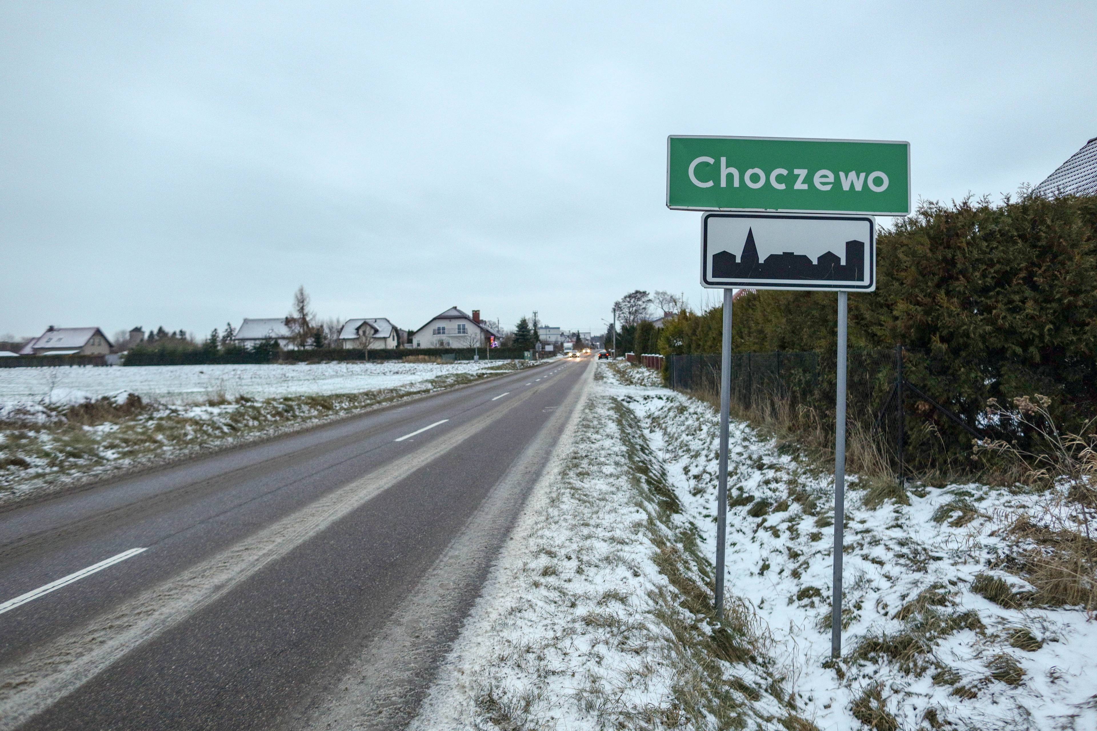 Wiejska szosa zimą. Przy niej tablica z nazwą miejscowości: Choczewo