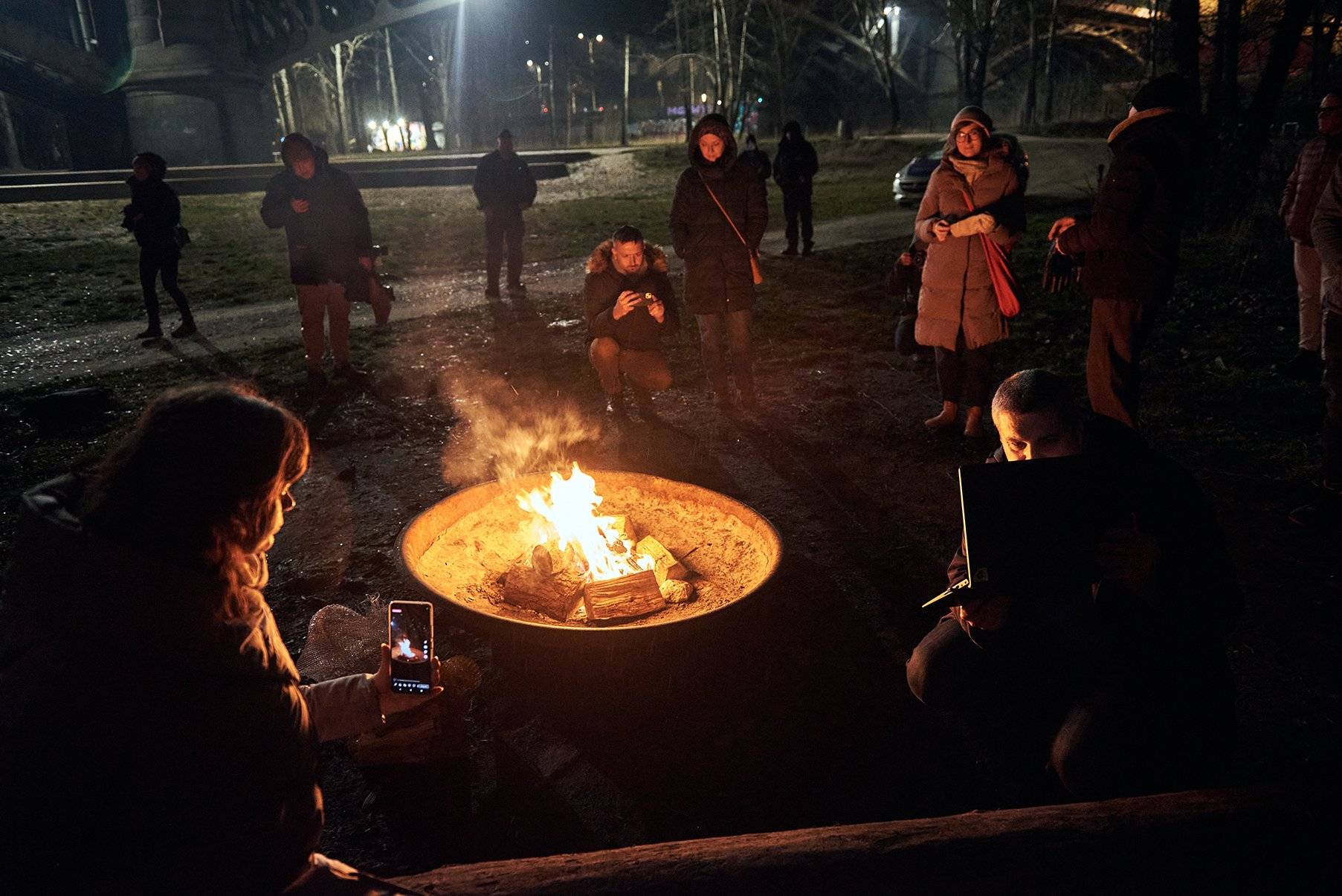 Ludzie wokół ognia w nocy - robią zdjęcia telefonami