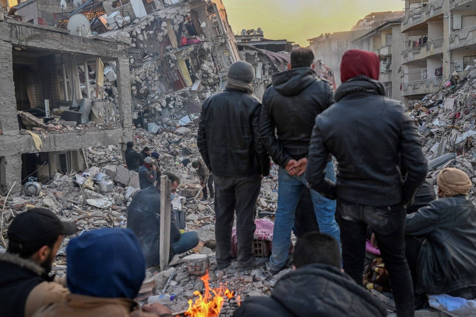 Grupa osób stoi tyłem, patrzą na ruiny kilkupiętrowych domów