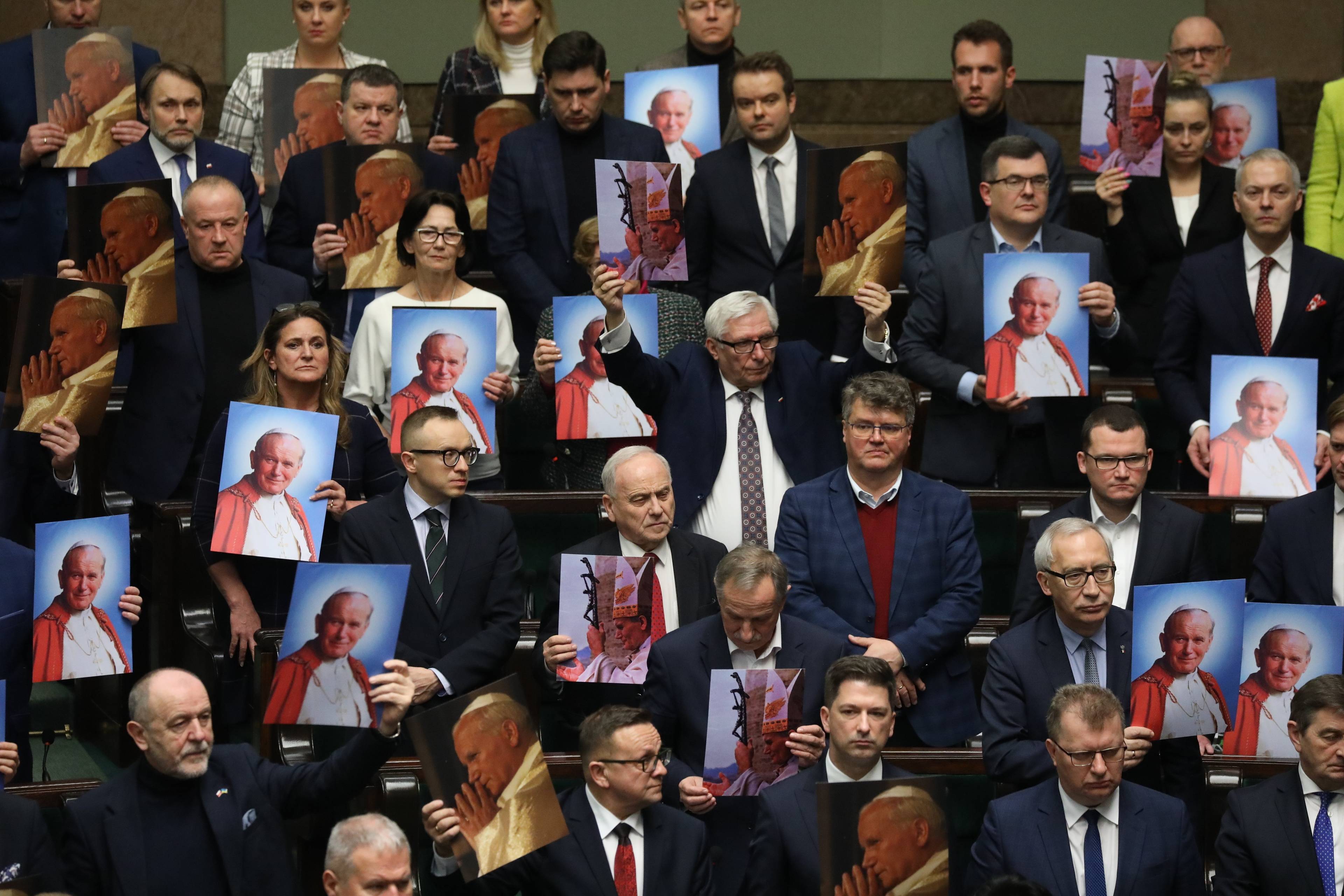 Posłowie PiS stoją na sali sejmowej z portretami Jana Pawła II