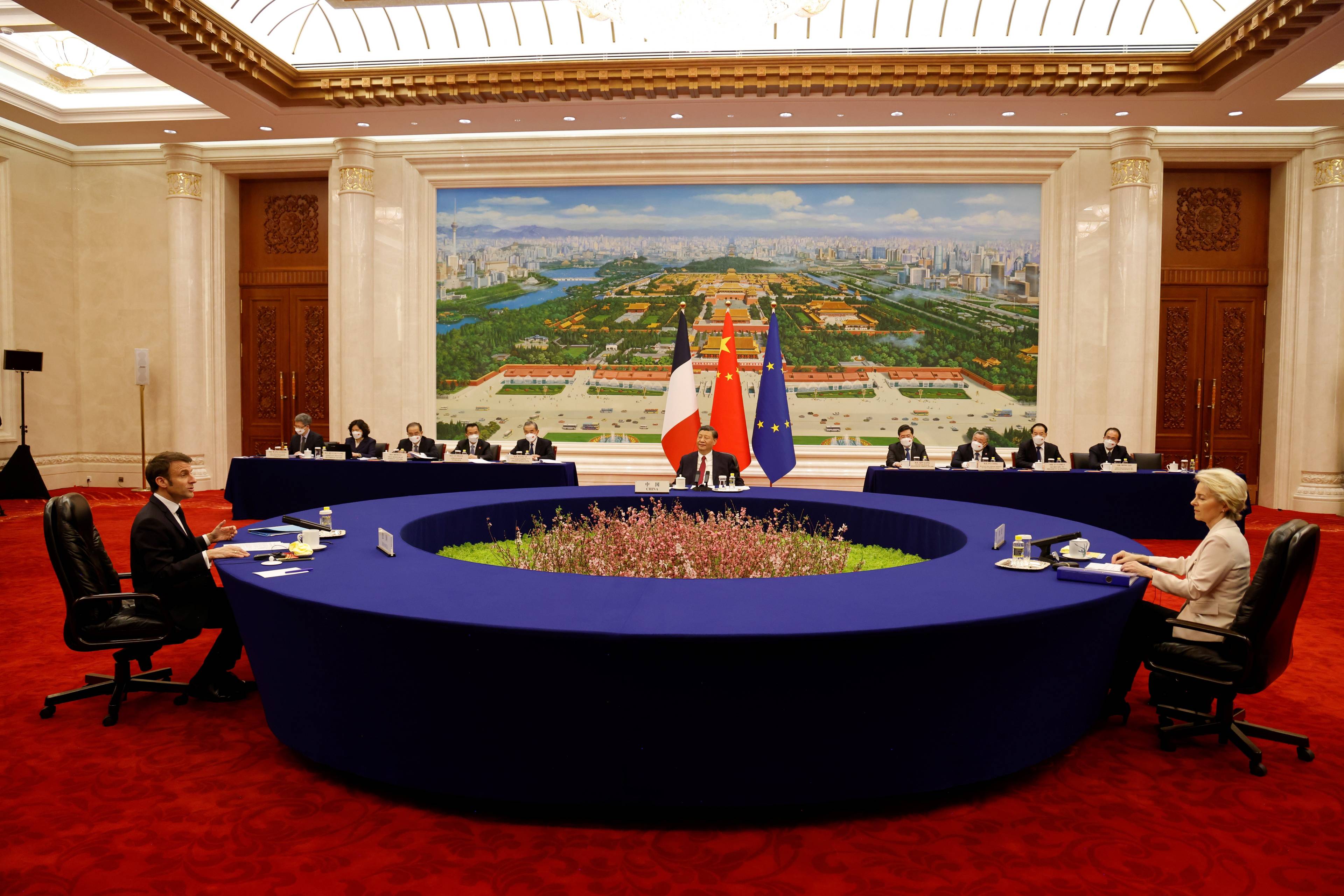 Przy wielkim okrytym ciemnoniebieską tkaniną okrągłym stole siedzą: kobieta i dwaj mężczyźni. W tle flagi Chin, Francji i Unii Europejskiej