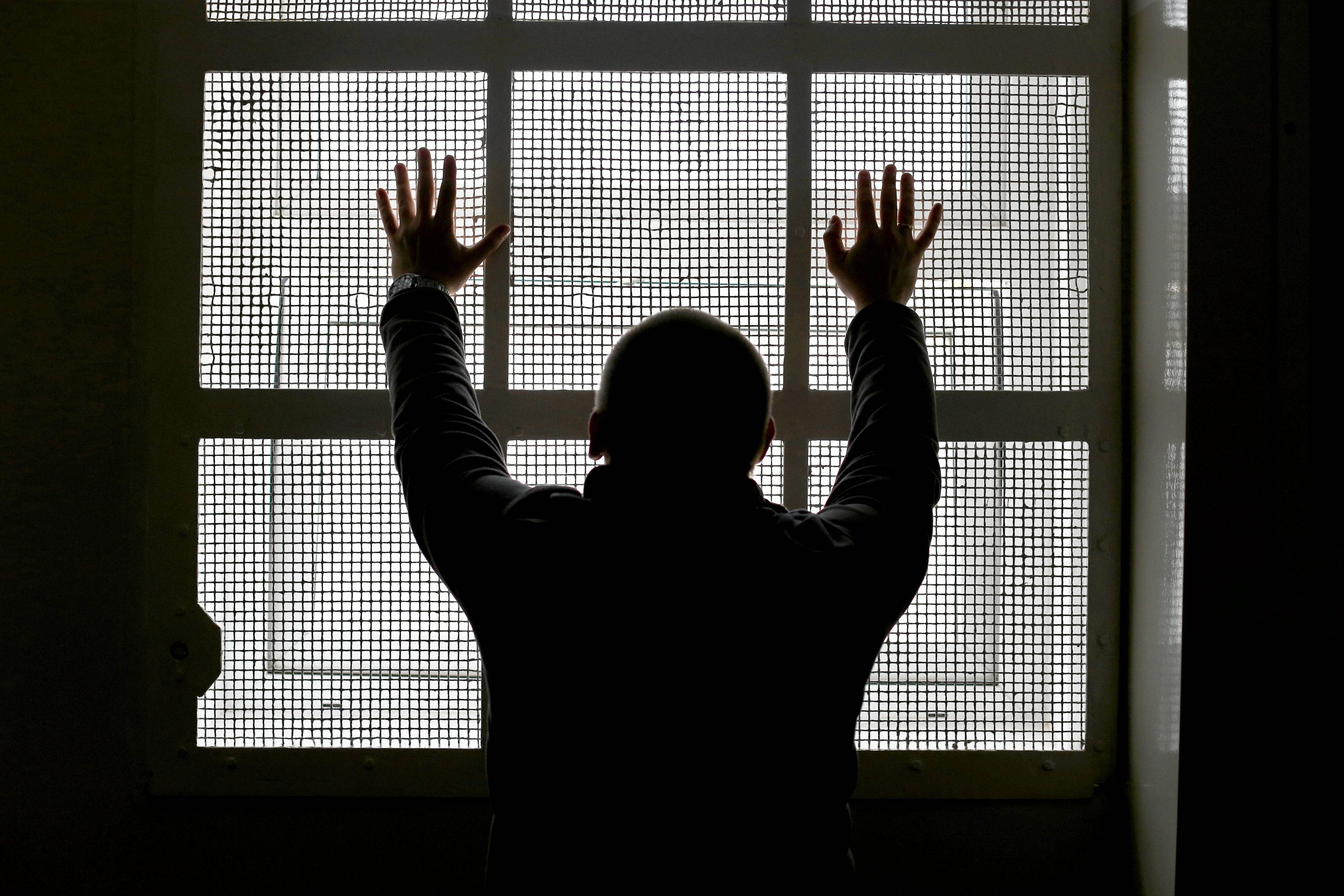 Mężczyzna stojący tyłem do obiektywu przy kracie więziennej