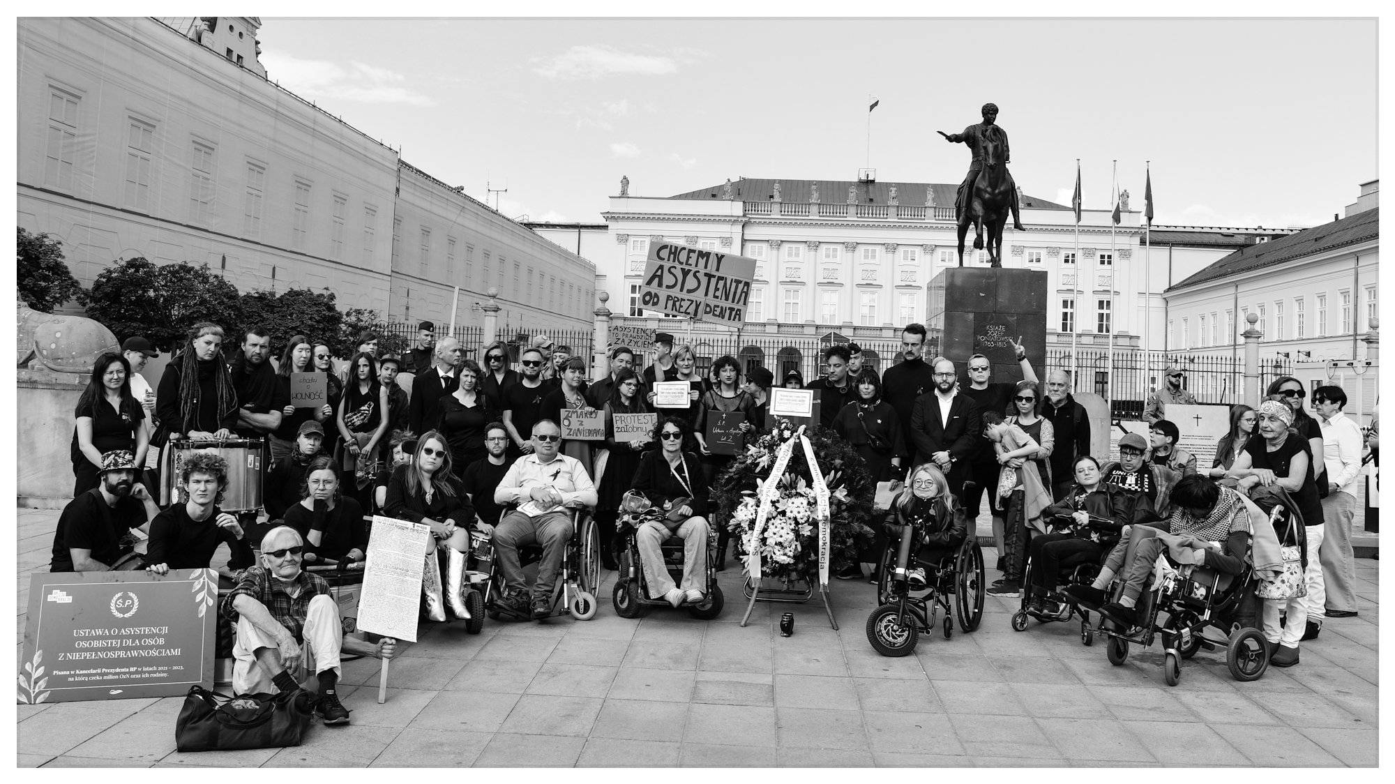 Czarno-białe zdjęcie grupowe pod Pałacem Prezydenckim. W pierwszym szeregu - osoby z niepelnosprawnościami