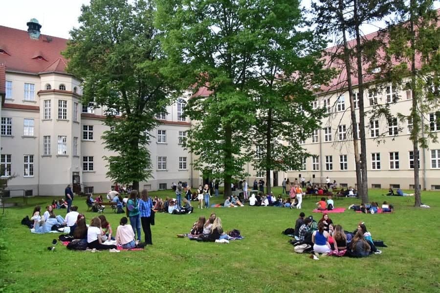uczniowie siedzą na trawie przed szkołą