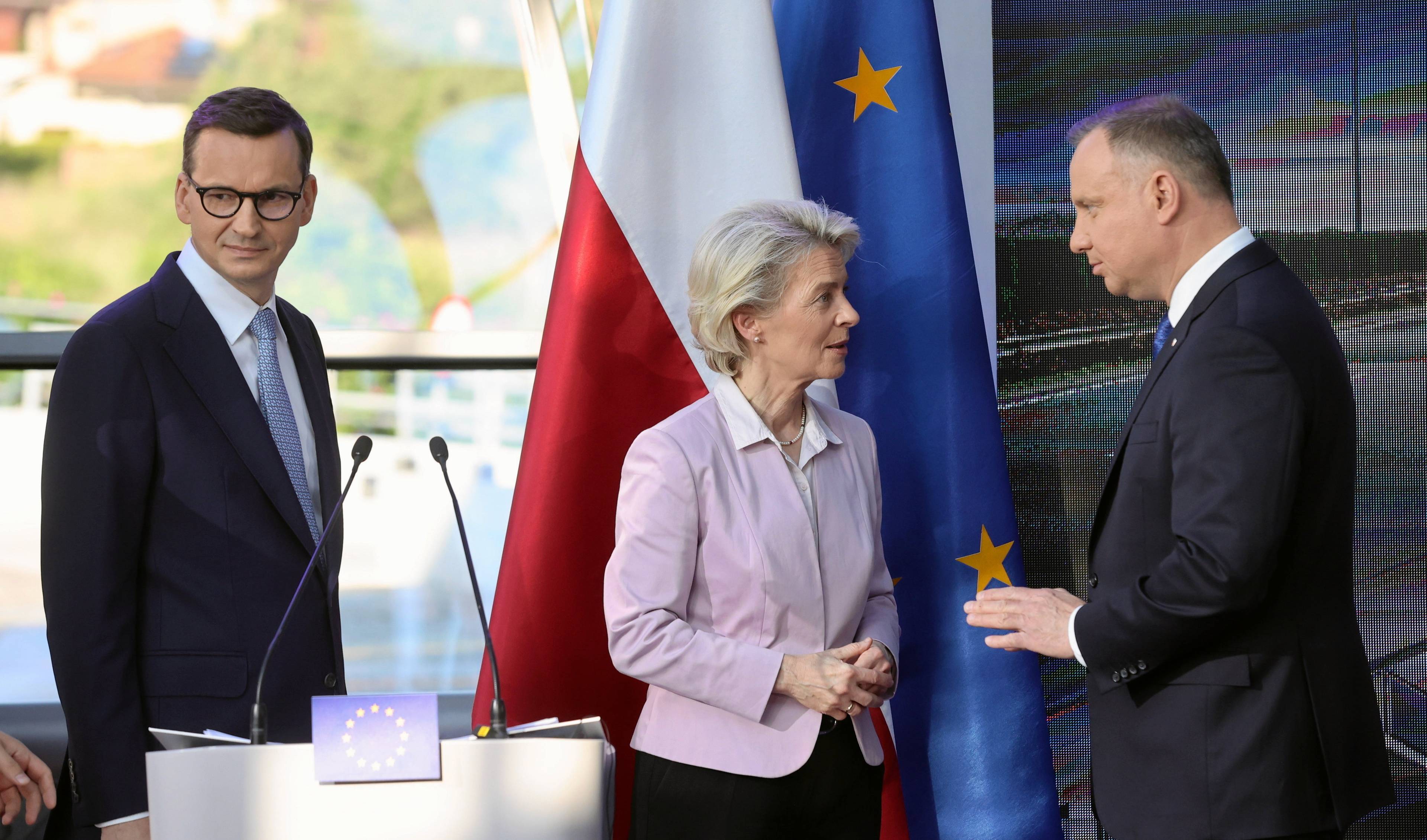 Mateusz Morawiecki, Ursula von Der Leyen i Andrzej Duda rozmawiają przy mównicy. Kobieta stoi w środku, za nimi flagi Unii Europejskiej i Polski