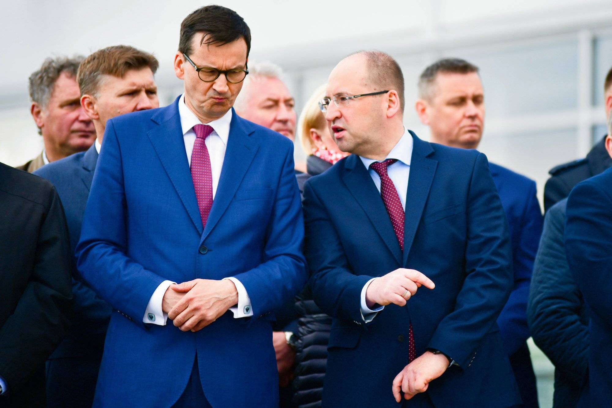 Premier Mateusz Morawiecki ze zirytowaną miną słucha, co mówi do niego stojący po lewej Adam Bielan.