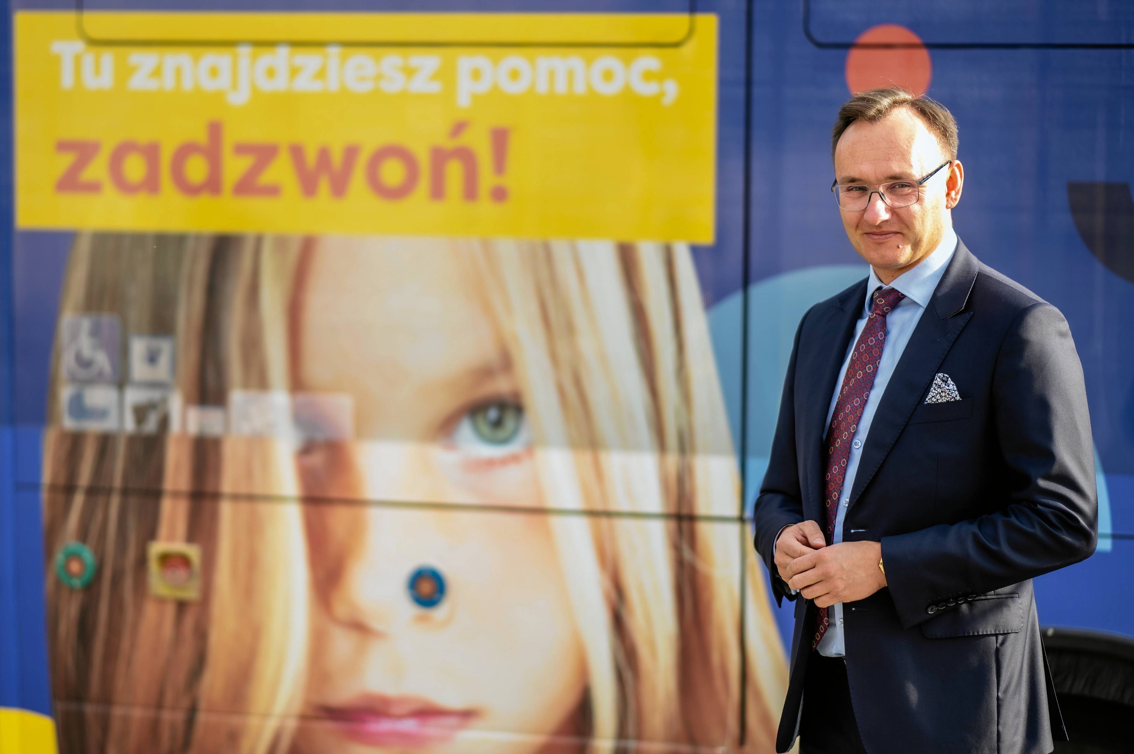 Na zdjęciu rzecznik praw dziecka Mikołaj Pawlak na tle baneru informującego o telefonie zaufania dla dzieci i młodzieży.