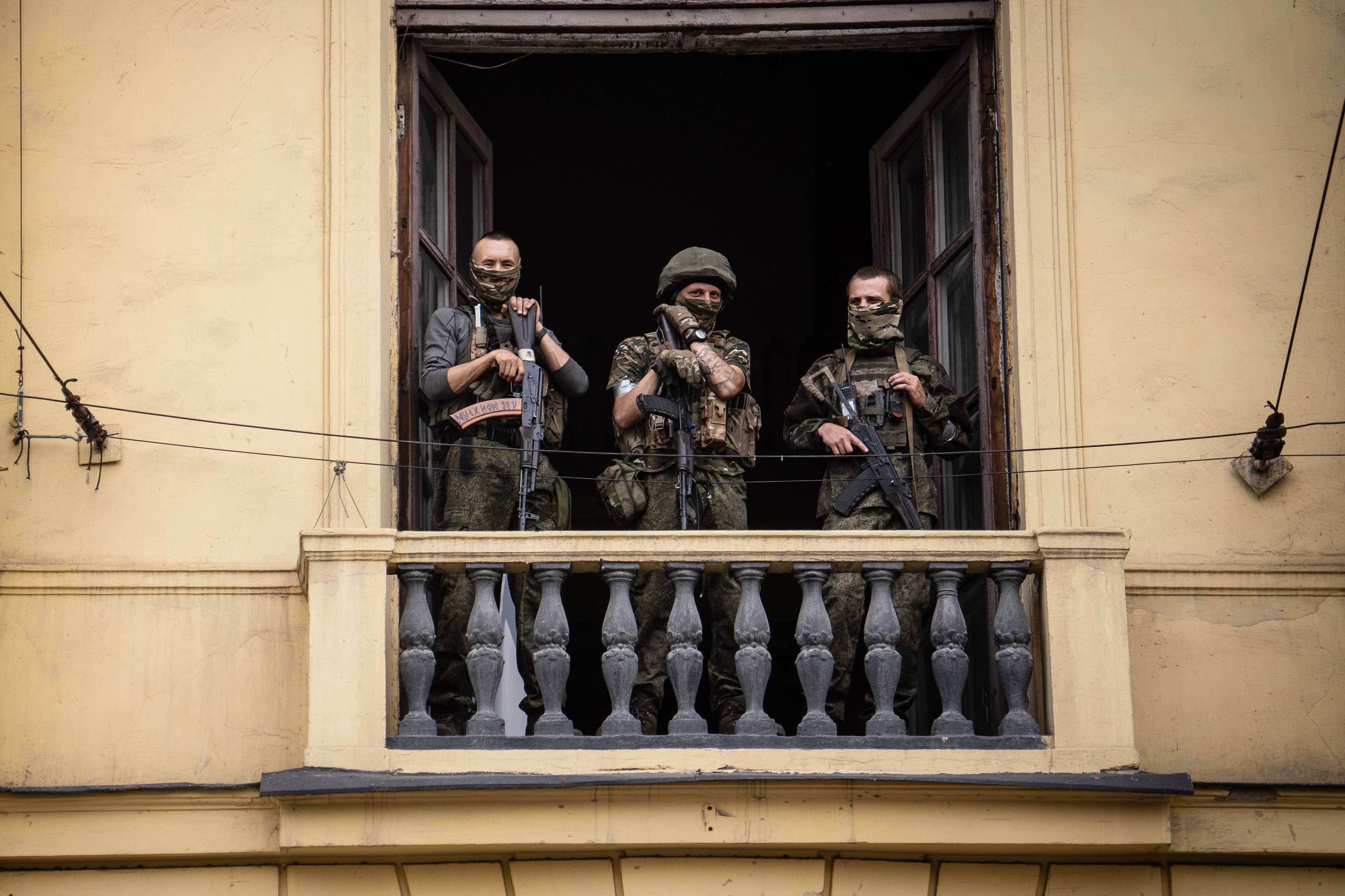 trzech żołnierzy w rynsztunku bojowym mierzy z długiej broni stojąc na balkonie klasycyzującego budynku