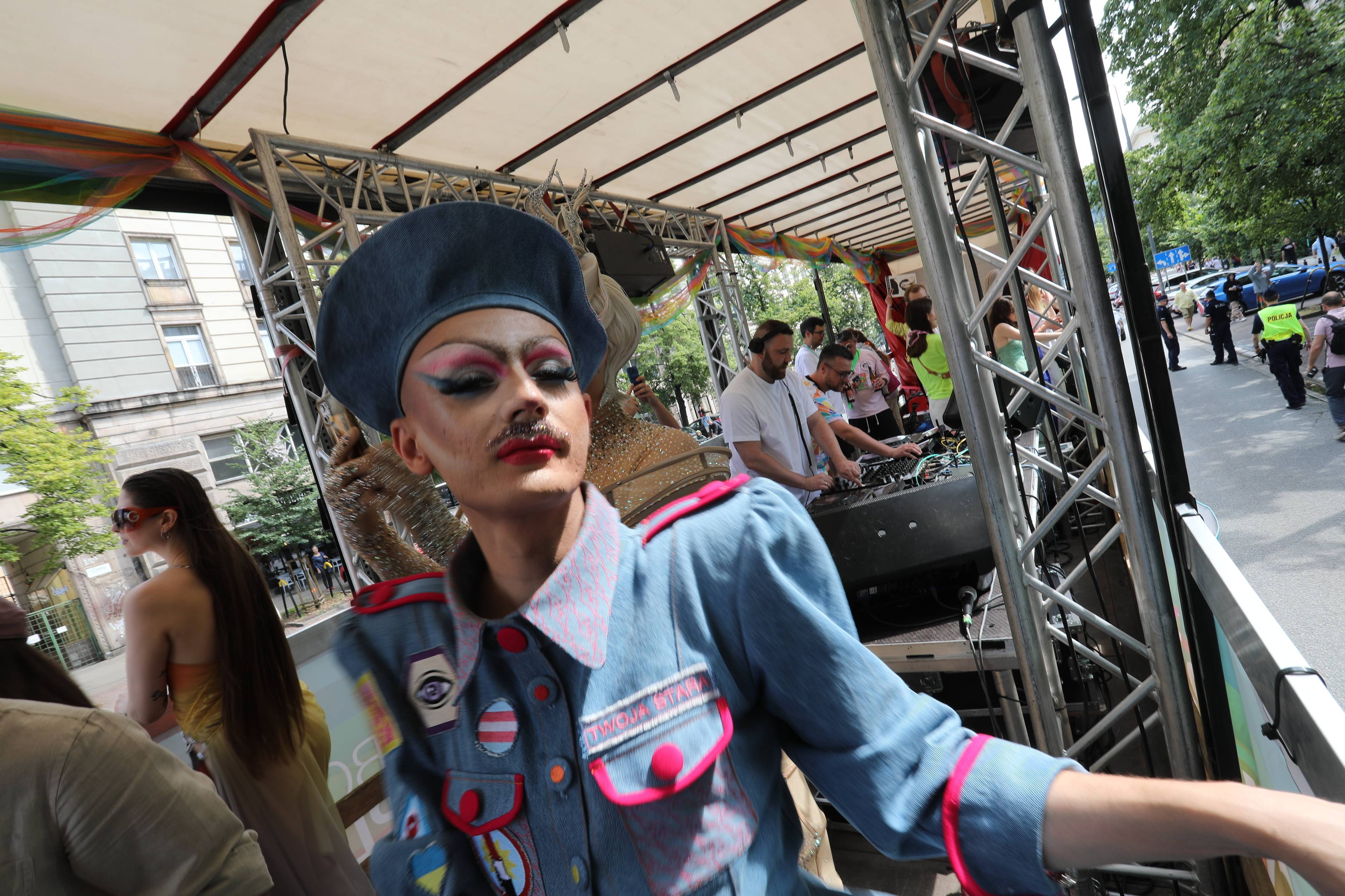 drag queen w czapce i z mocnym makijażem stoi na platformie jadącej w Paradzie