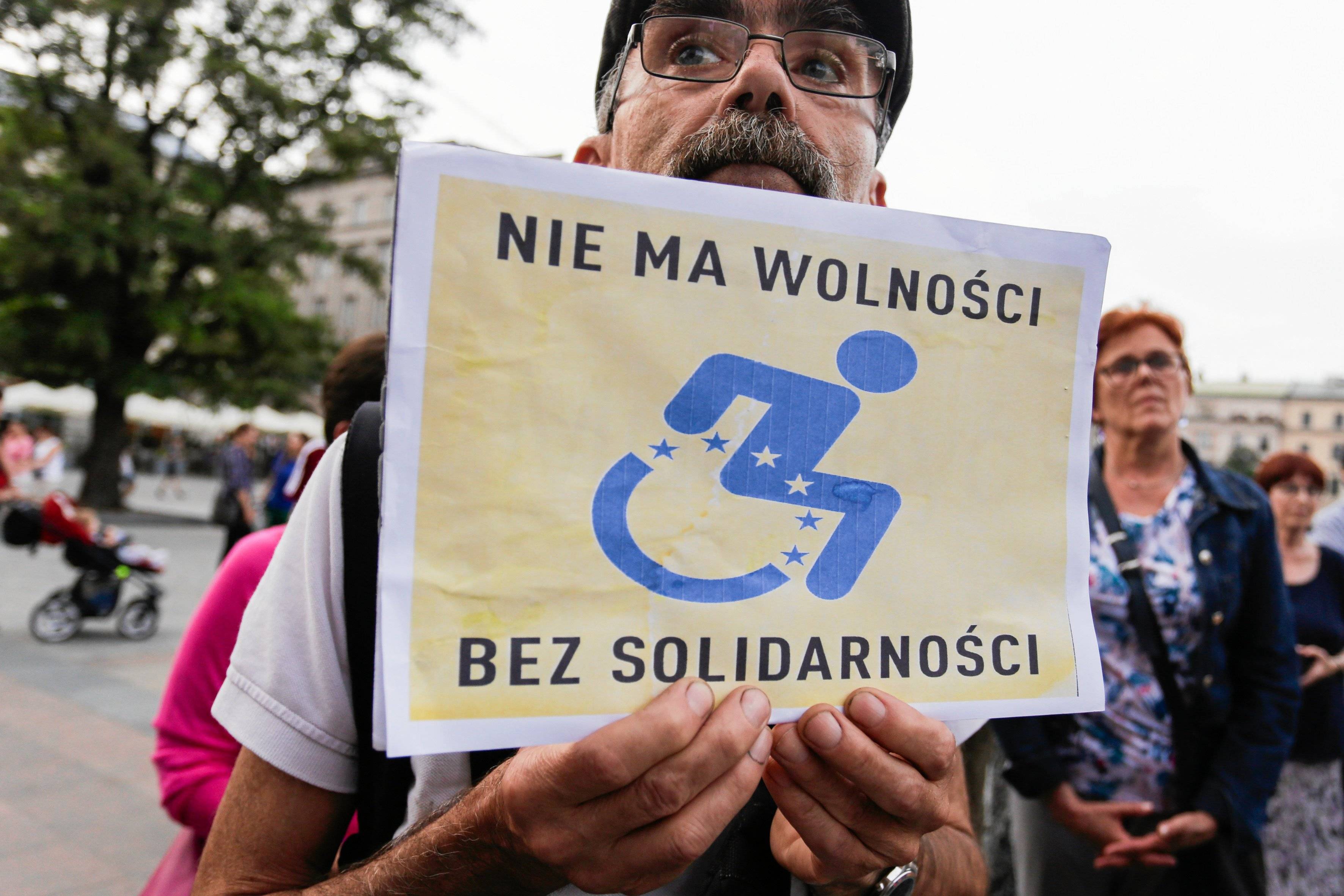 Mężczyzna trzyma plakat z napisem "Nie ma wolności bez solidarności" i rysunkiem wózka inwalidzkiego