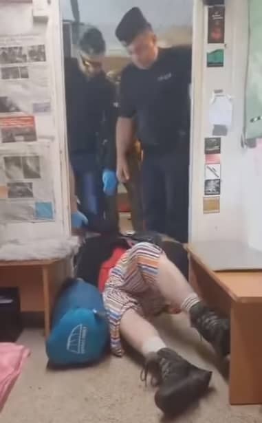 dwóch mężczyzn w mundurach policji stoją w drzwiach, jedna osoba leży na ziemi