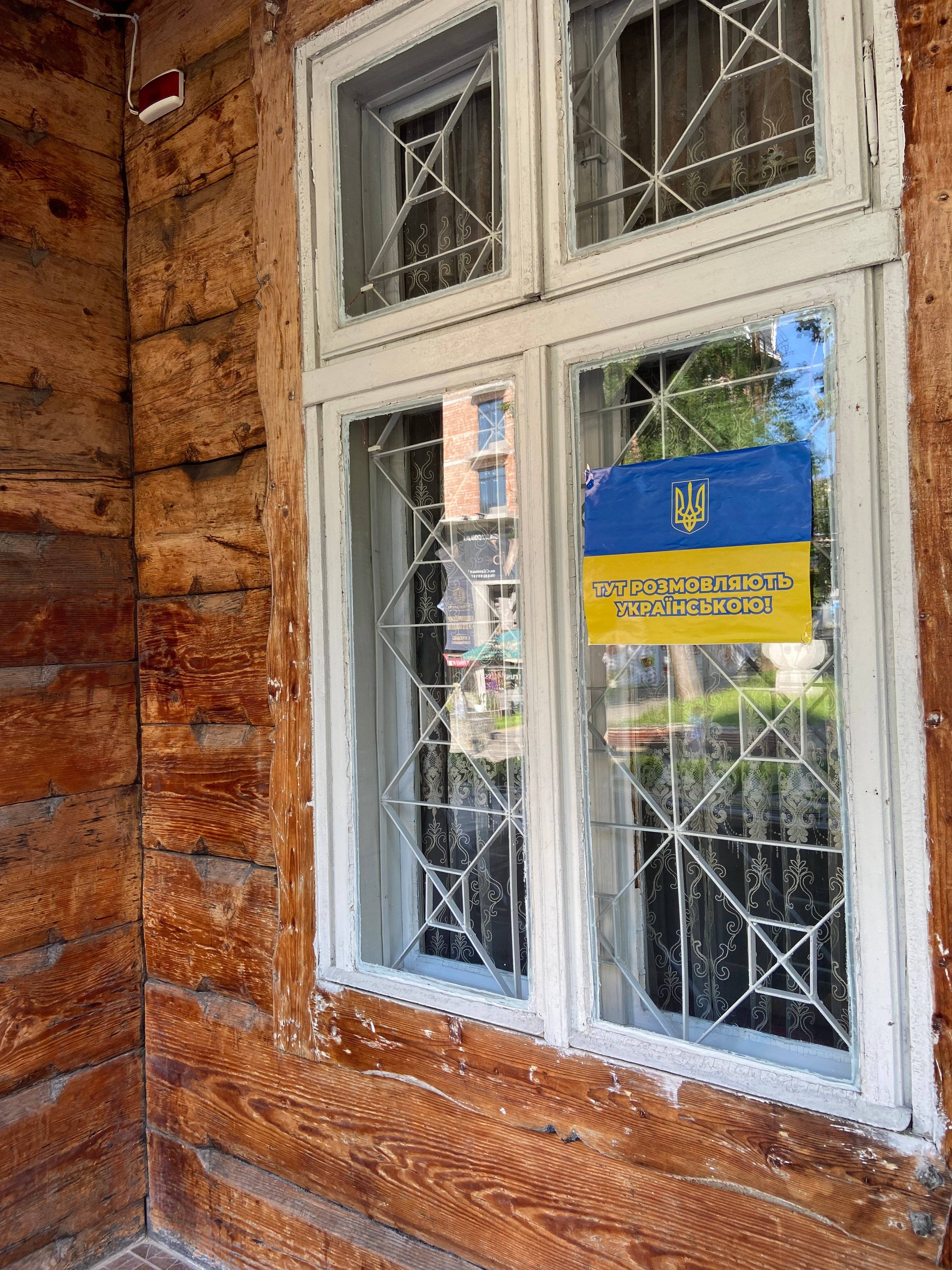Okno drewnianego domu z kartką niebiesko-żółtą z informacją po ukraińsku, tu rozmawiamy po ukraińsku