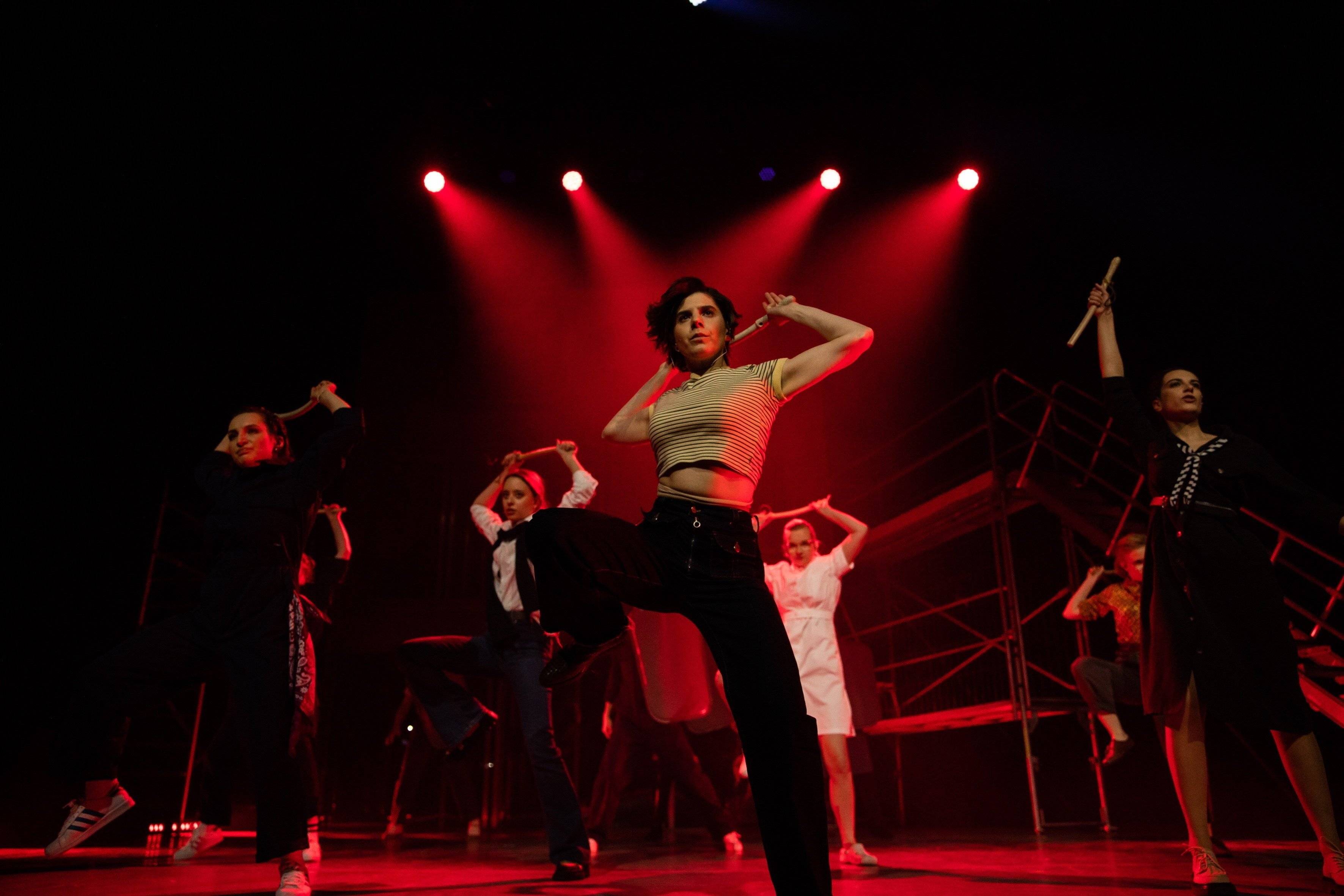 cena z musicalu „1989” - aktorki tańczą na tle snopów czerwonego światła.
