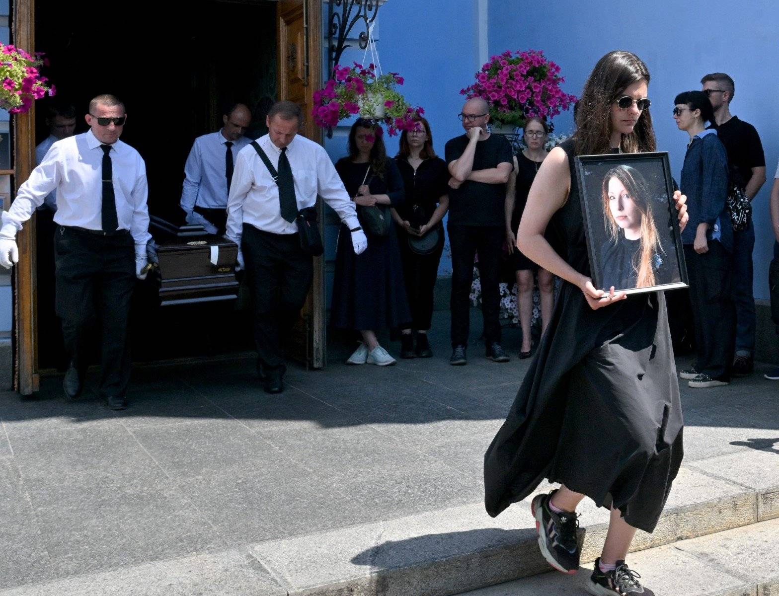 A woman holds a picture of Victoria Amelina, as pallbearers carry her coffin at the end of her funeral ceremony in Mykhaylo Gold Domes in Kyiv on July 4, 2023. - A Ukrainian writer and war crimes investigator was wounded and then died in a Russian missile strike last week  when a Russian missile destroyed the Ria Pizza restaurant in the eastern city of Kramatorsk on Tuesday, killing 12 people, including children, and wounding dozens. (Photo by Sergei SUPINSKY / AFP)