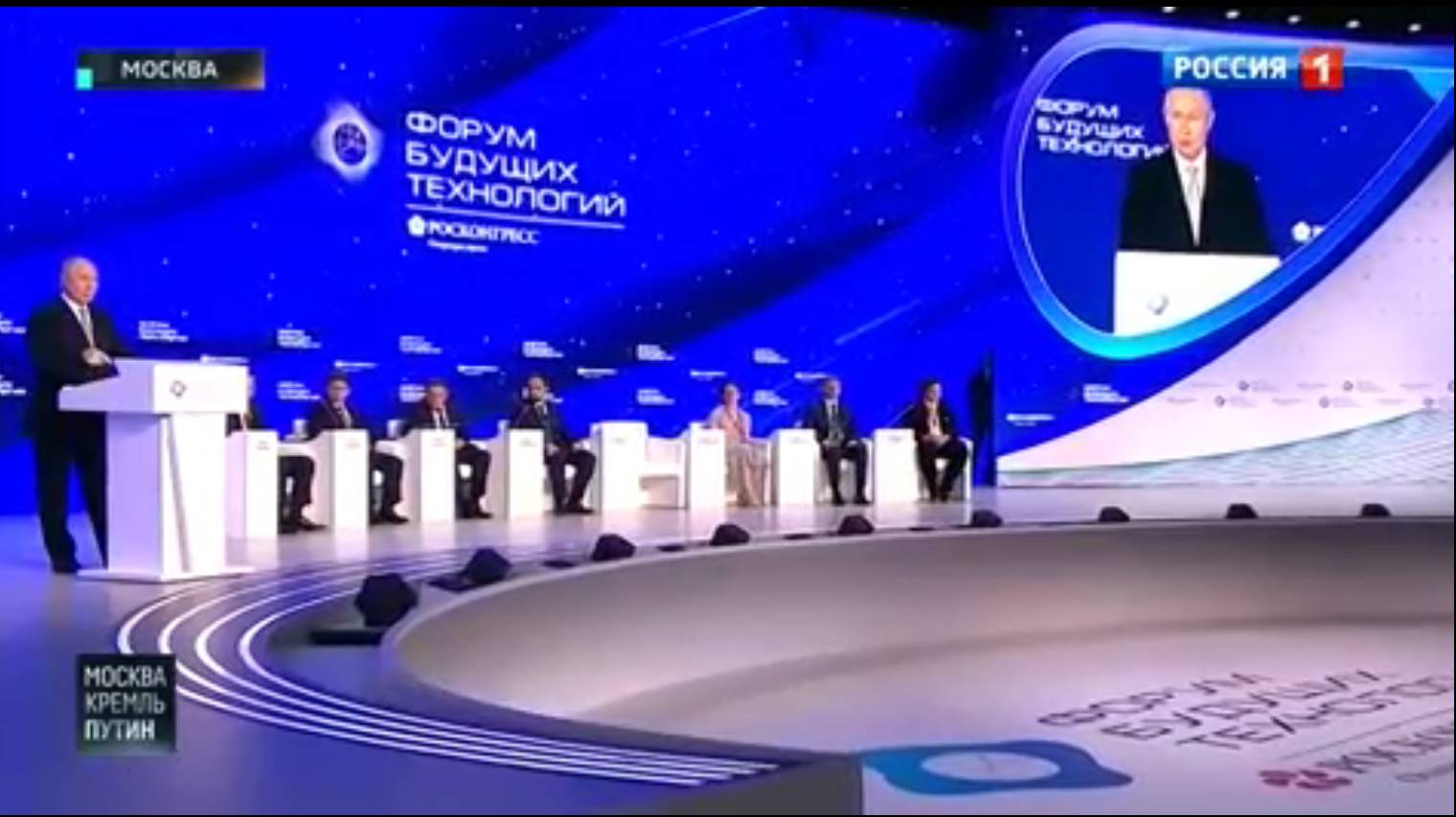 Putin uczestniczy w panelu dyskusyjnym na wielkiej scenie z niebieskim tłem