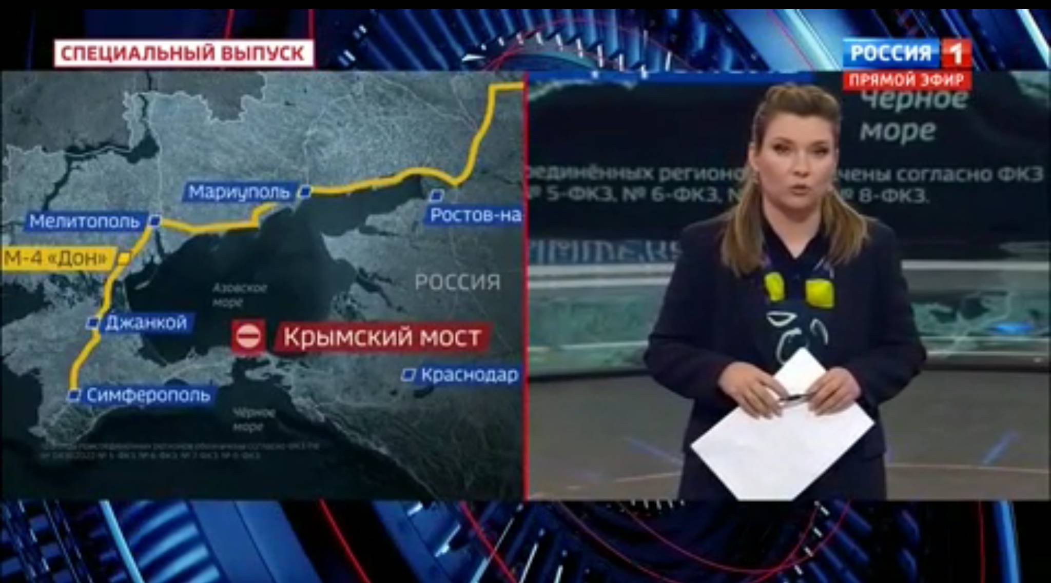 Kobieta w studiu telewizyjnym stoi przed mapą pokazuącą objazd z Krymu do Rosji z pominięciem mostu krymiskiego (dookoła Morza Azowskiego)
