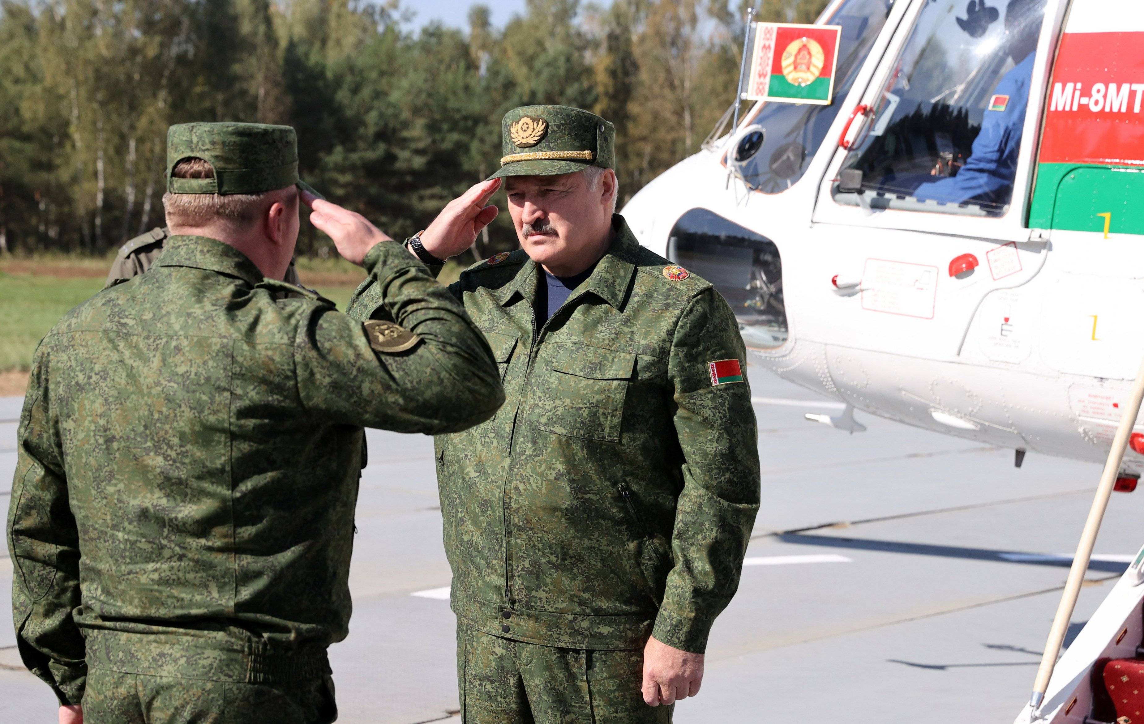 Aleksandr Łukaszenka w mundurze przyjmuje meldunek białoruskiego żołnierza przed helikopterem Mi-8
