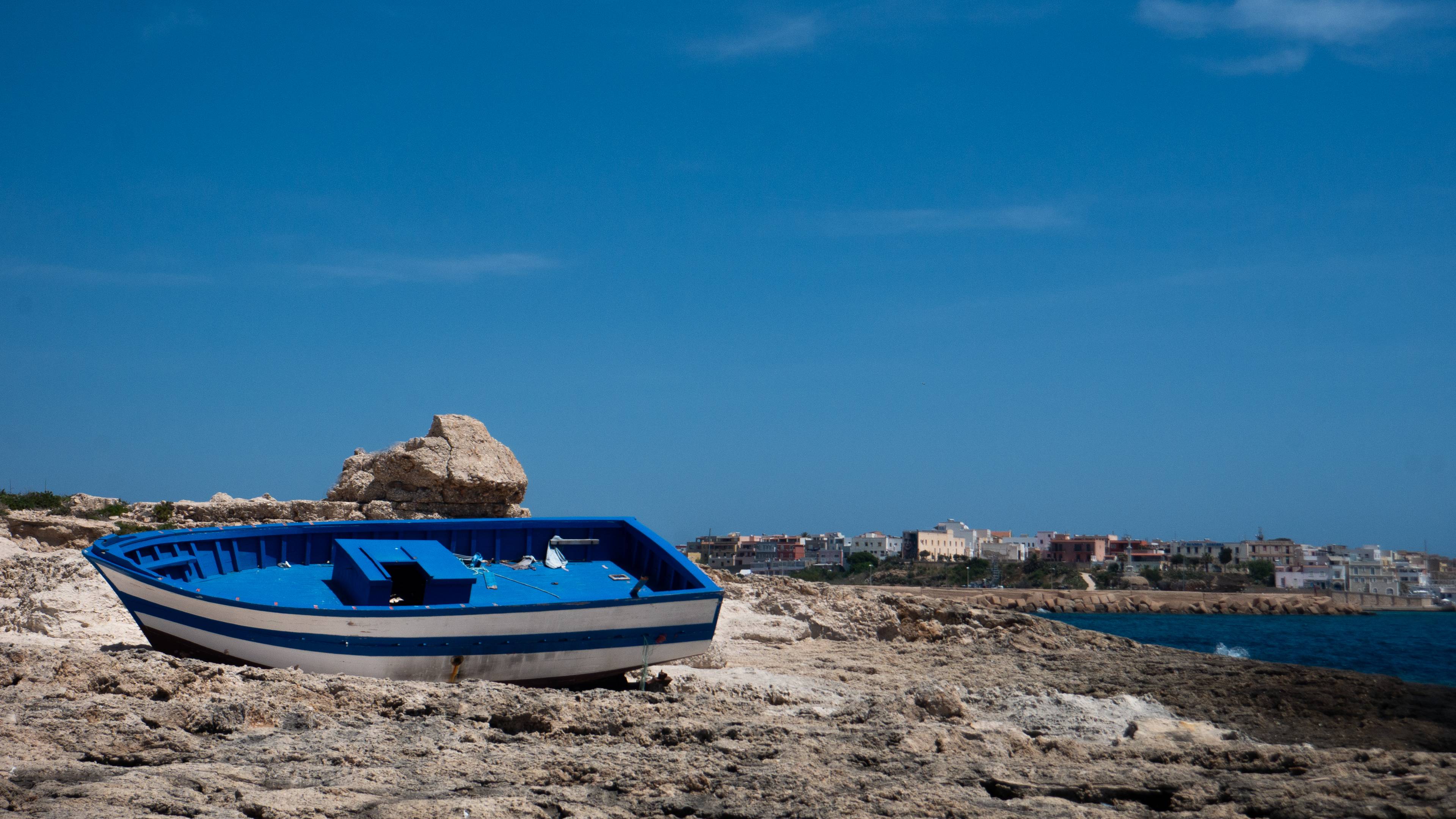 Łódź pomalowana na biało i niebiesko, leżąca na skałach na wyspie.