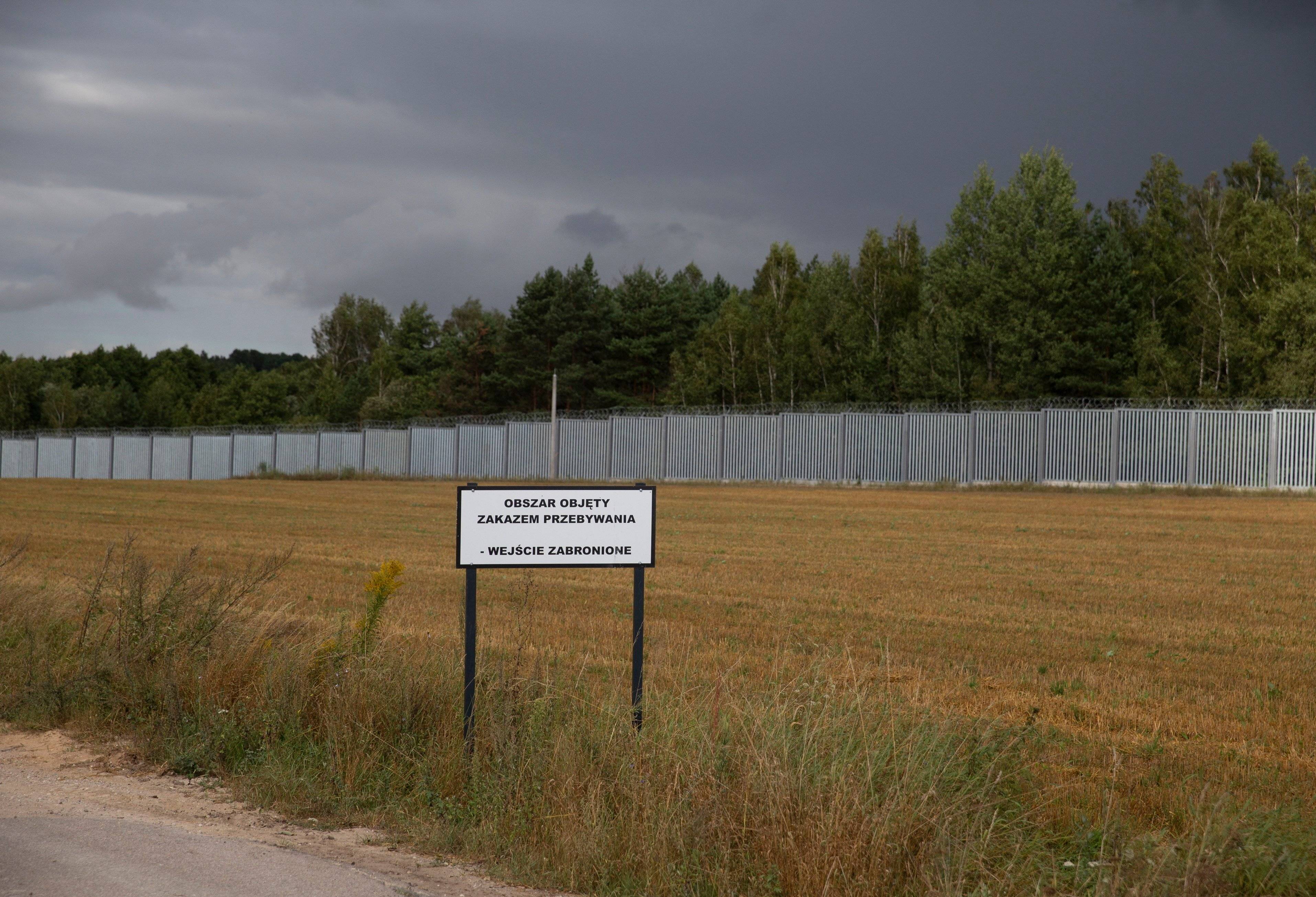 Granica polsko-białoruska: wielki płot, a z przodu tablica z napisem "Obszar objęty zakazem przebywania"