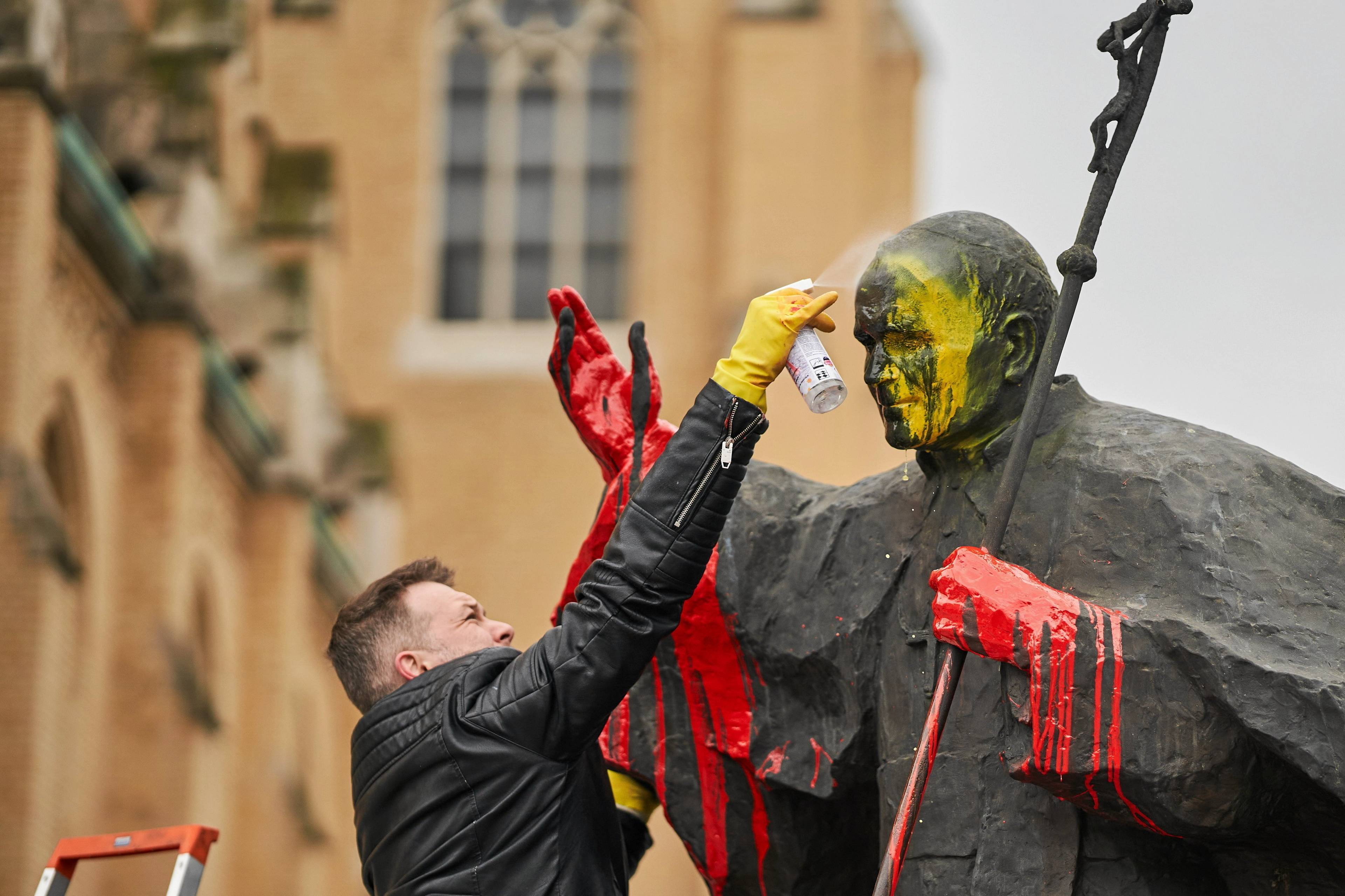 mężczyzna czyści pomnik papieża z żółtej farby
