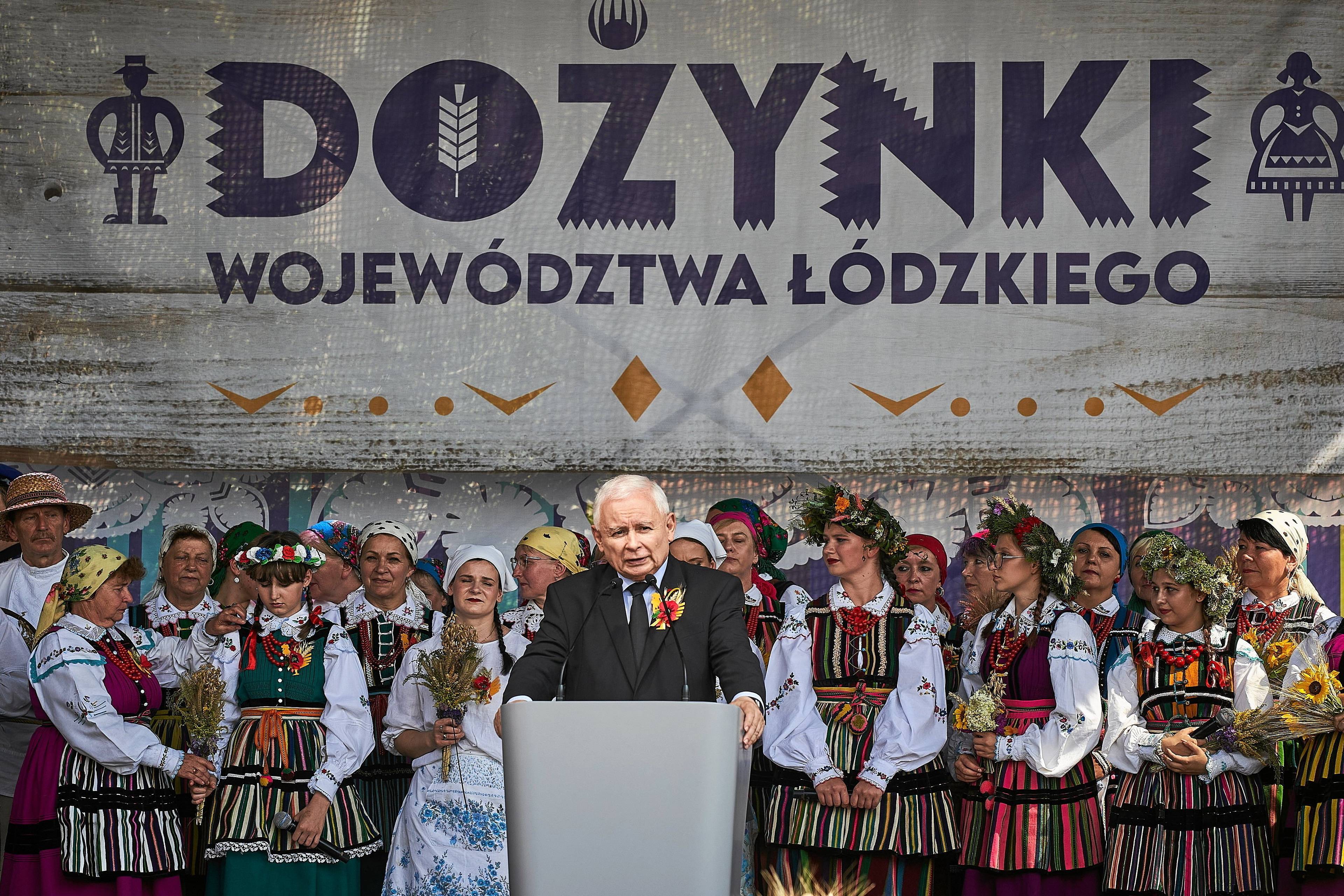 Jarosław Kaczyński przemawia pod wielkim napisem "Dożynki województwa łódzkiego". W tle kobiety w strojach ludowych.