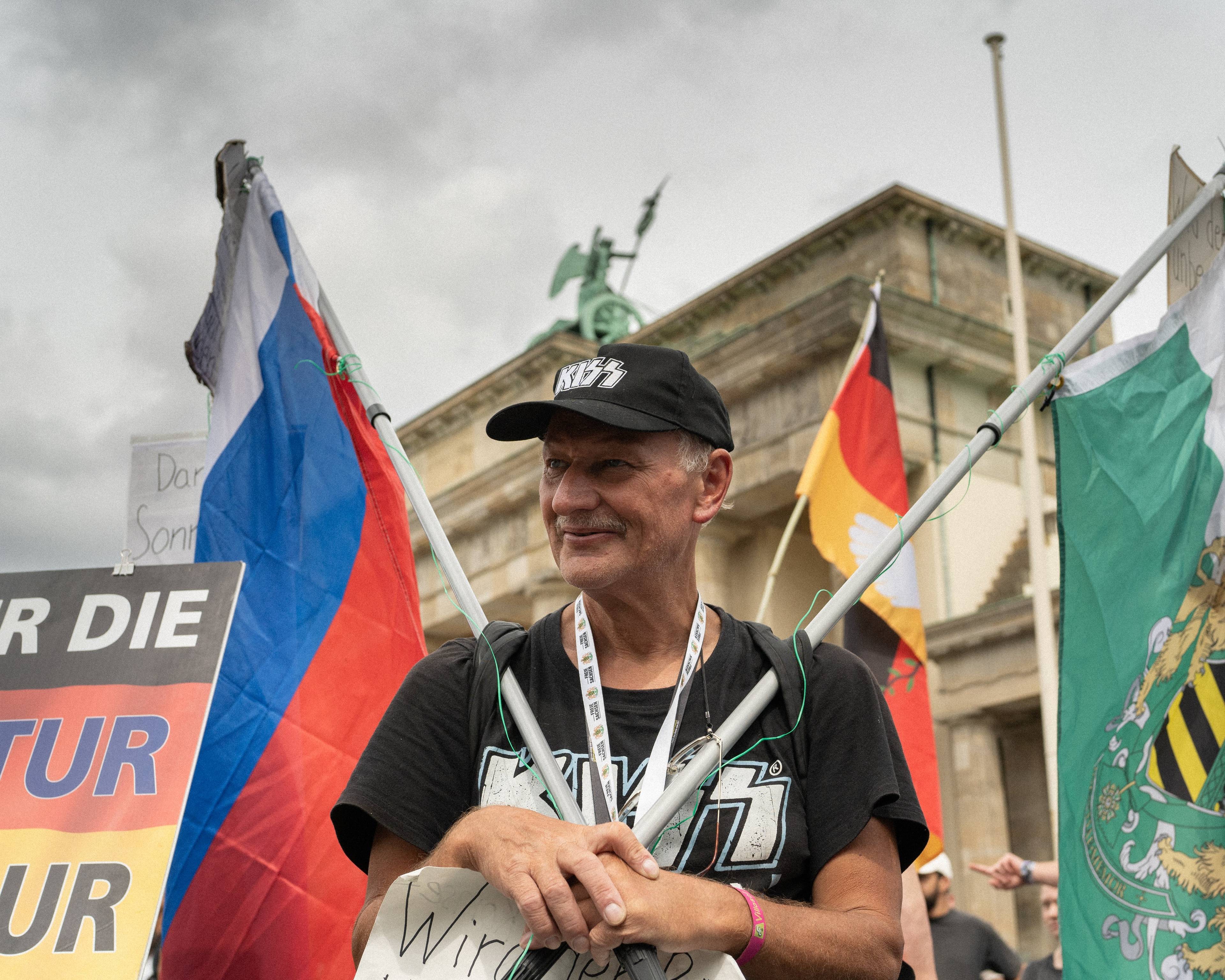 mężczyzna w czapce z daszkiem trzyma dwie flagi, rosyjską i saksońską