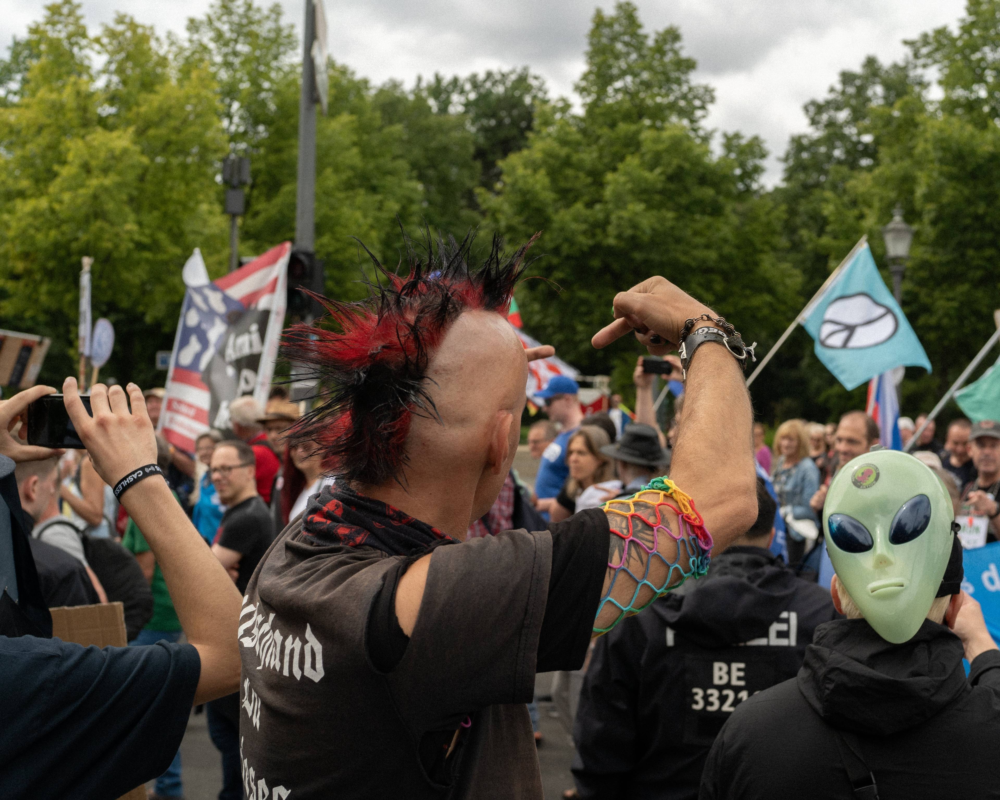 Mężczyzna z kolorowym "irokezem" na głowie pokazuje środkowy palec przechodzącym demonstrantom