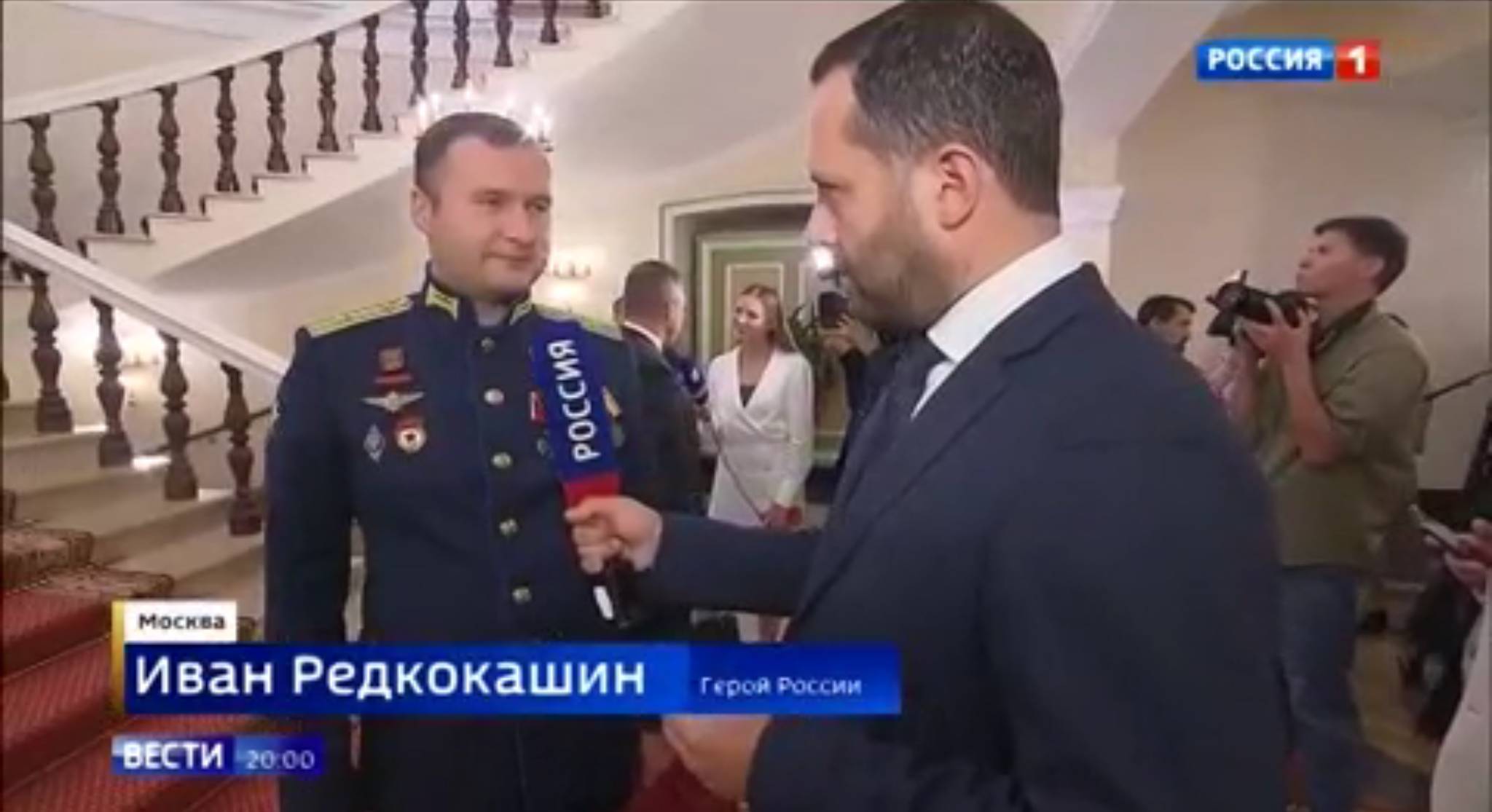 Męzczyzna w galowym rosyjskim mundurze z odznaką pilota mówi do mikrofonu "Wiesti"