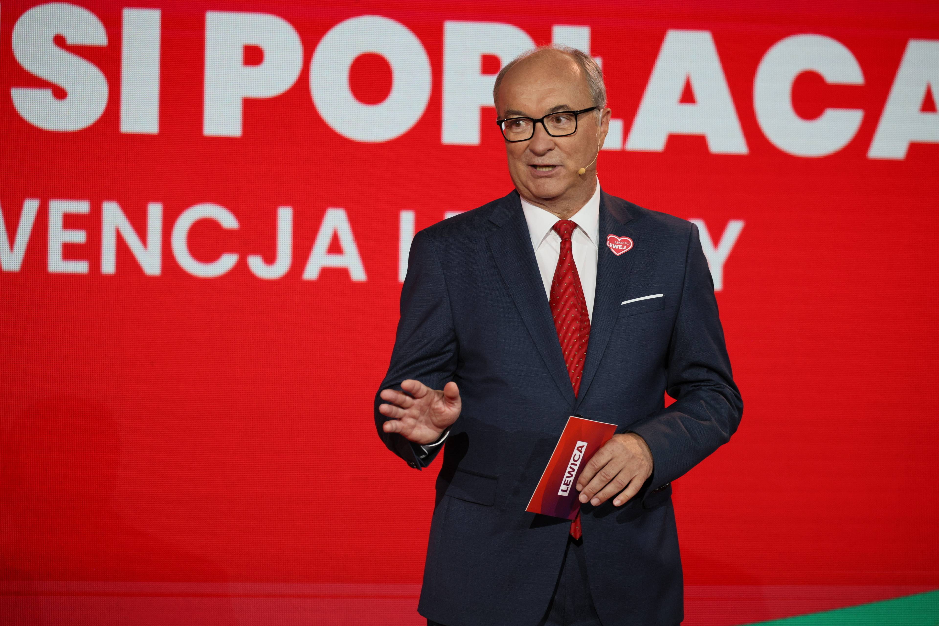 Współprzewodniczący Lewicy Włodzimierz Czarzasty przemawia na scenie na czerwonym tle z wyciągniętą do przodu prawą ręką